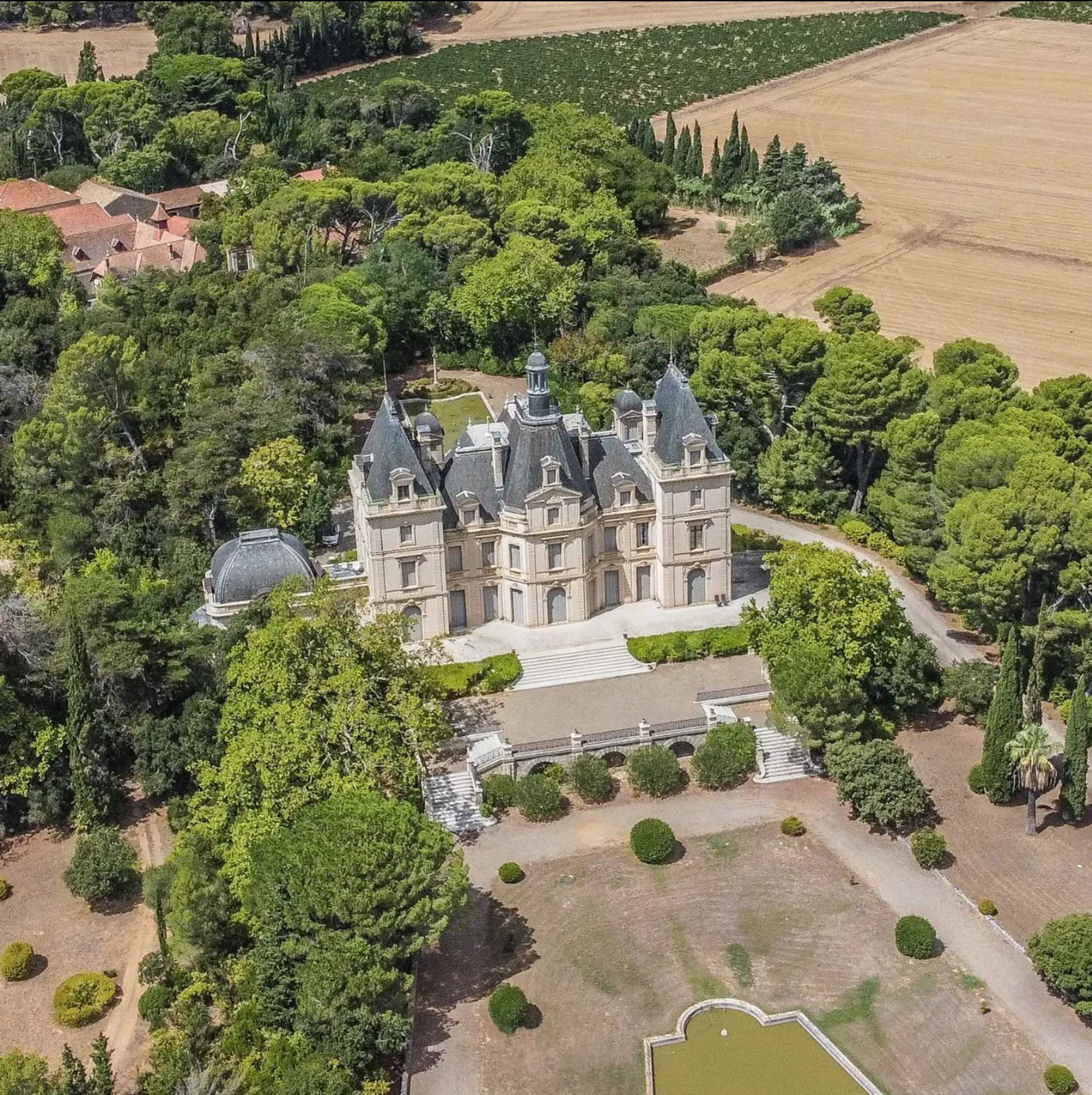 Aerial view of a Second Empire chateau with mansard roofs, turrets, formal gardens, and ornamental pond