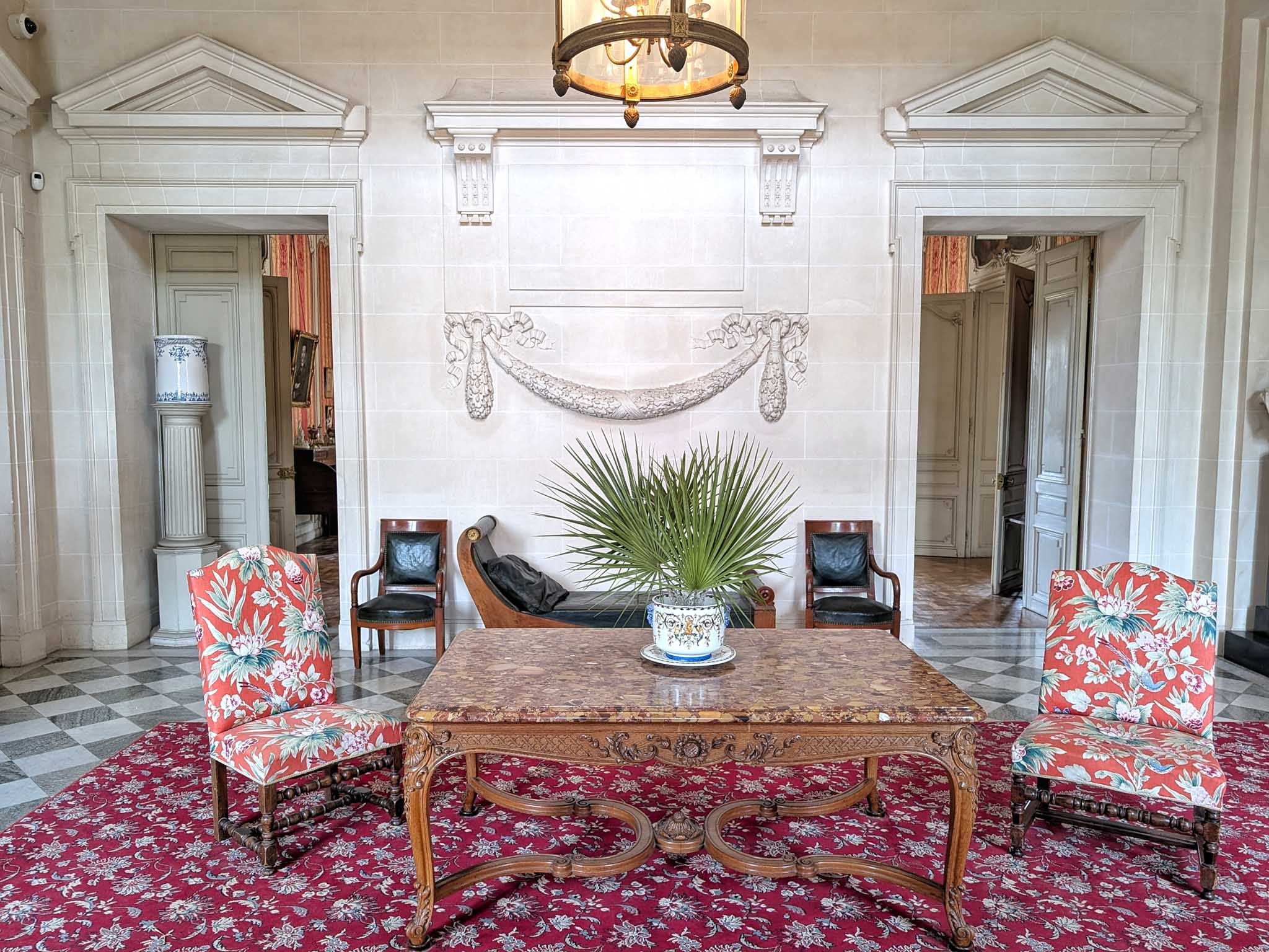 Classical French chateau interior room with carved walnut table, checkered marble floor, and lantern chandelier