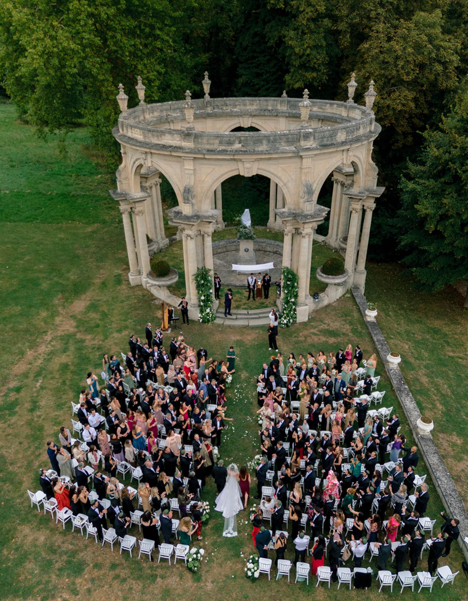 Aerial view of 200-guest ceremony at neoclassical stone rotunda with white chair rows and florals