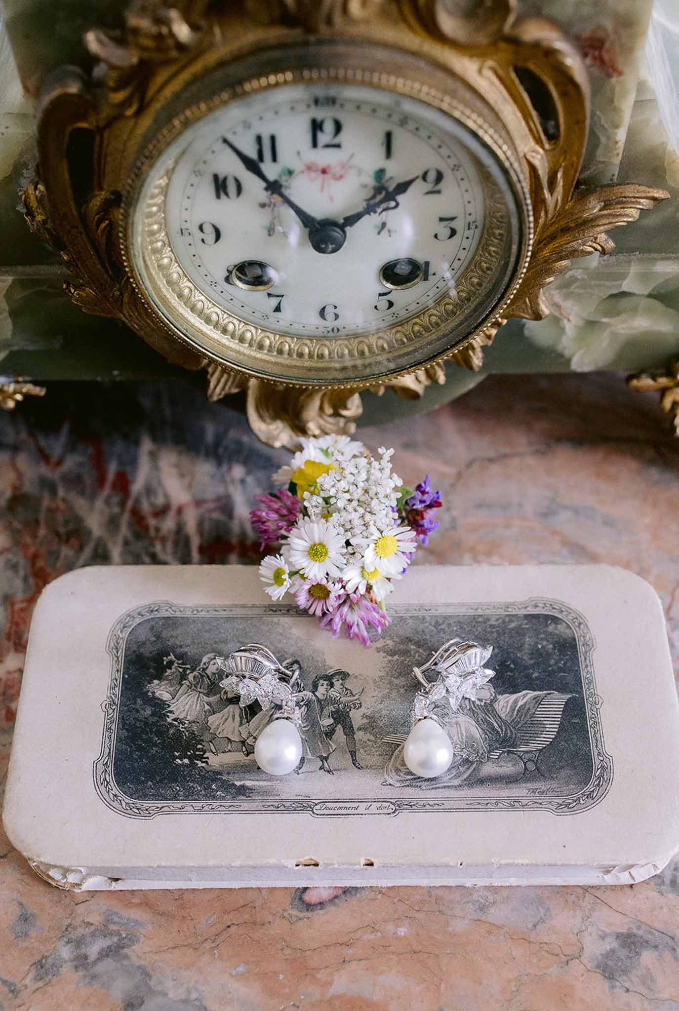 Pearl drop earrings on vintage French card box with wildflowers and antique ormolu clock on pink marble