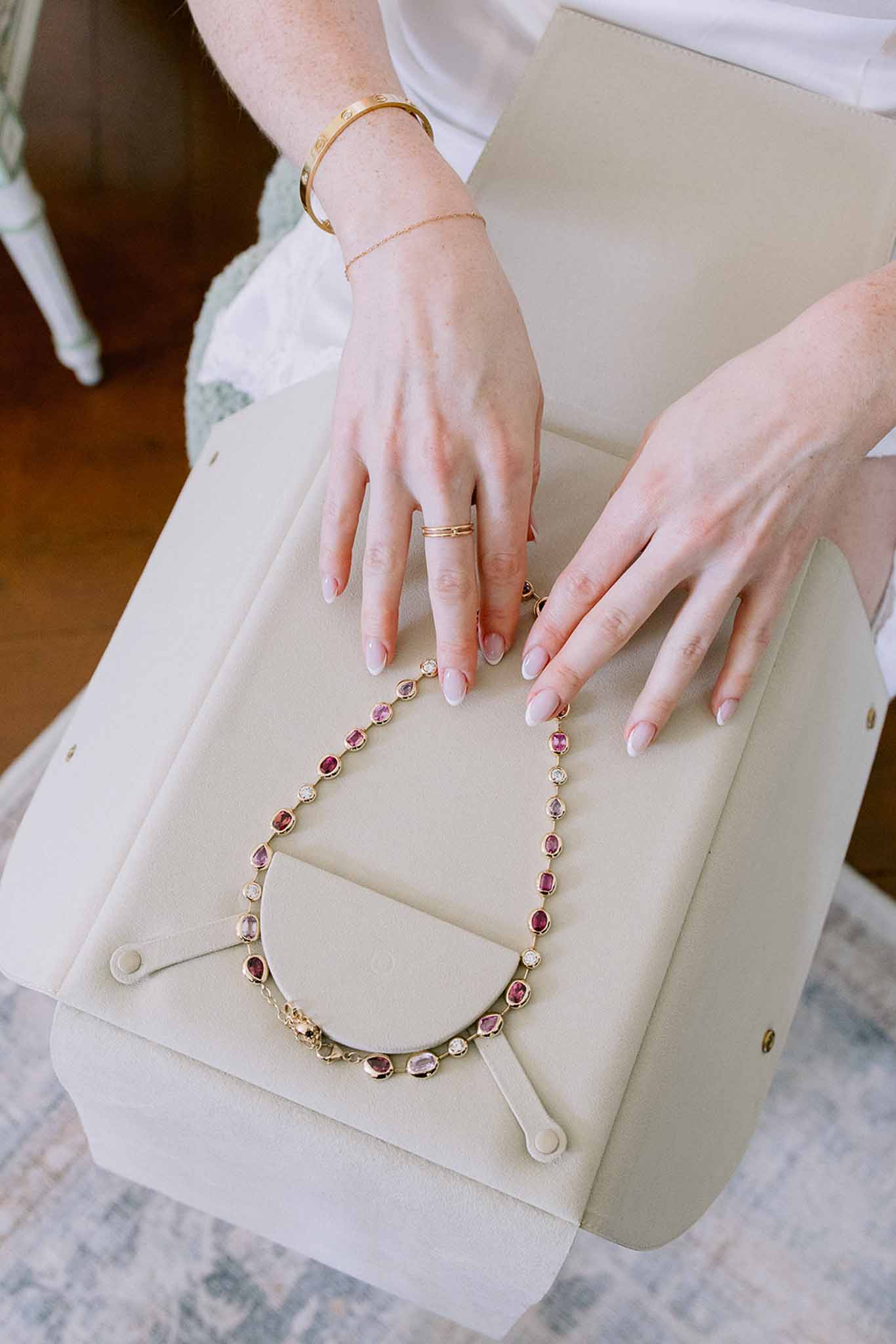 Bride's hands on cream clutch with gold ruby necklace, Cartier bangle, and French manicure during getting ready
