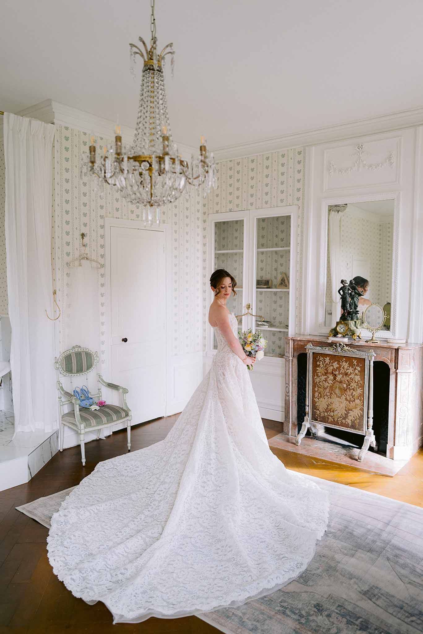 Bride in off-shoulder lace fit-and-flare gown with cathedral train holding yellow and white bouquet in chateau room
