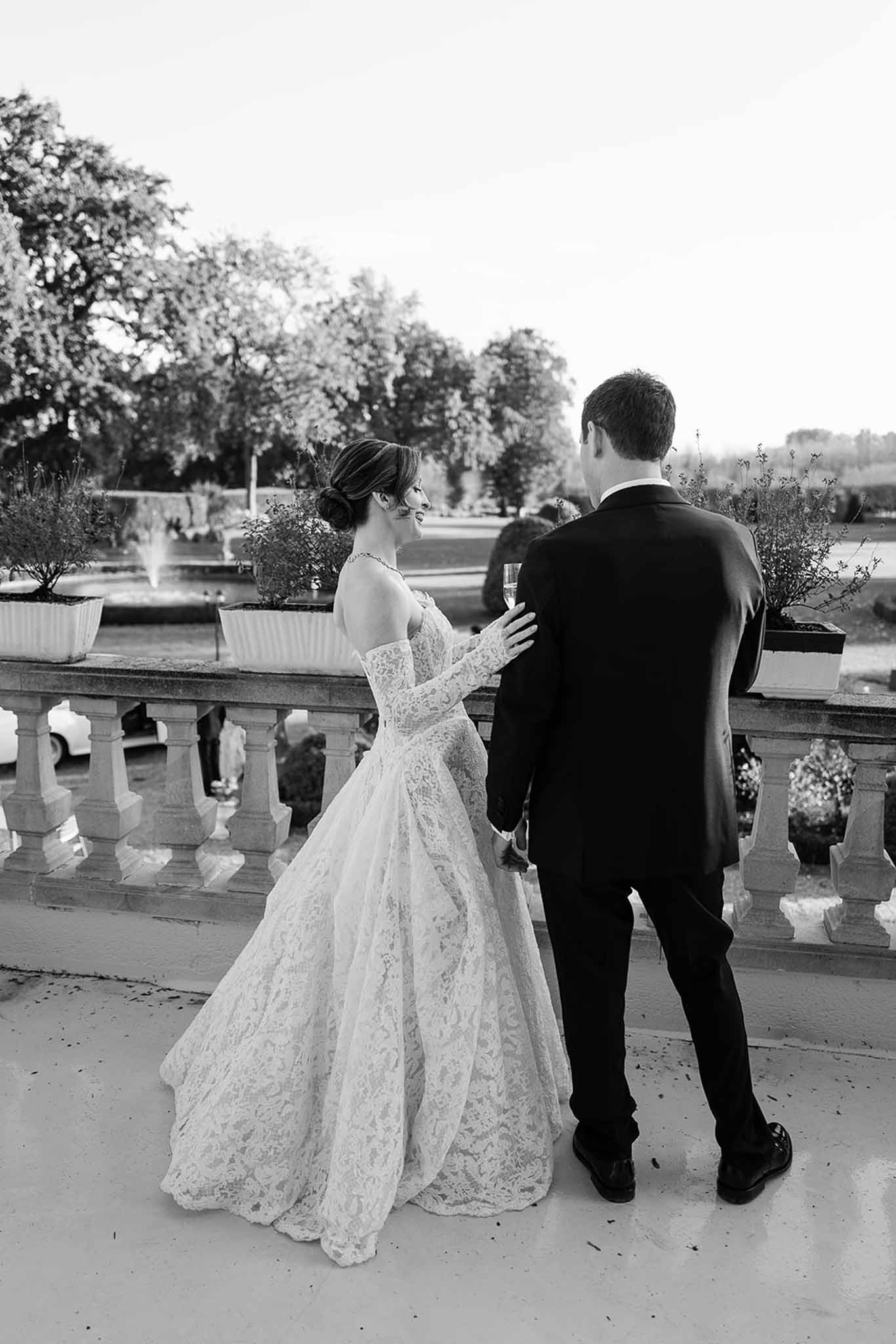 Black and white couple from behind on stone terrace bride in lace ballgown with gloves groom holding champagne flute
