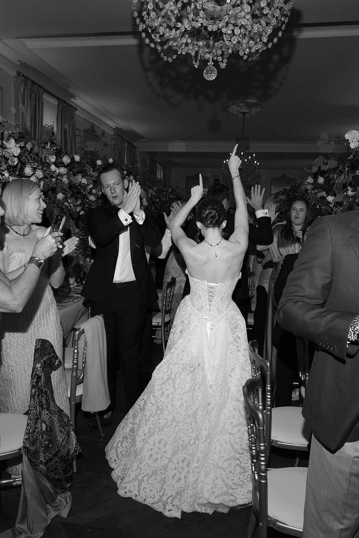 Black and white shot of bride arms raised and groom clapping during reception entrance in ballroom