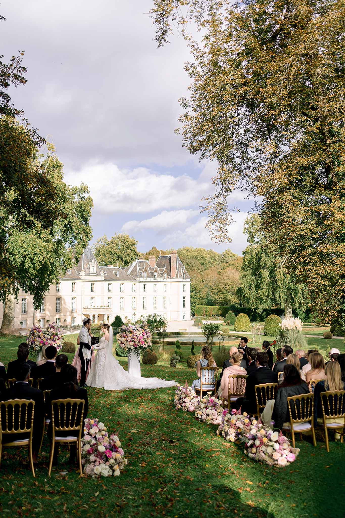 50-guest ceremony with blush and mauve aisle florals on lawn before white mansard-roofed chateau
