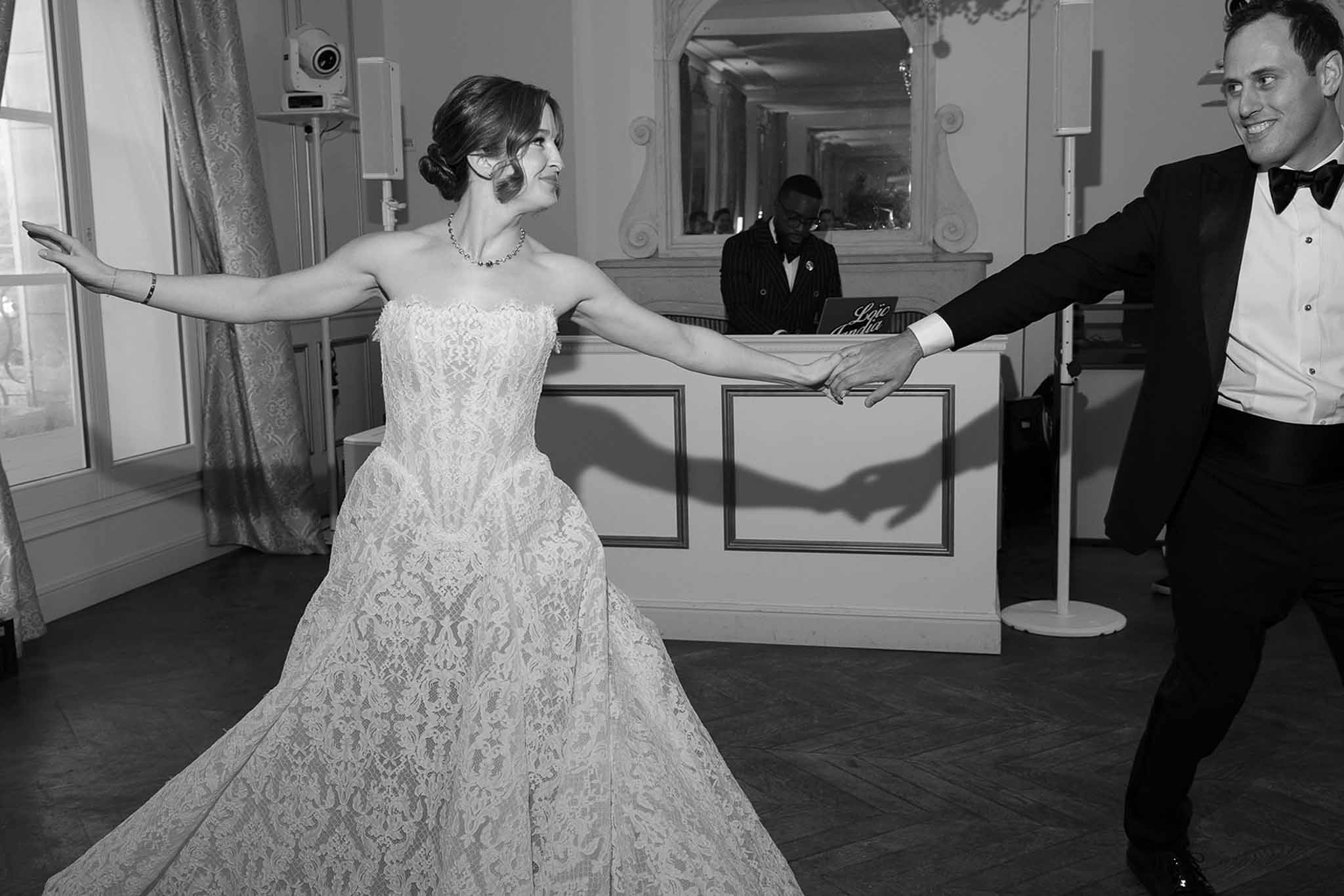 Black and white image of bride and groom performing first dance in formal ballroom with DJ booth behind