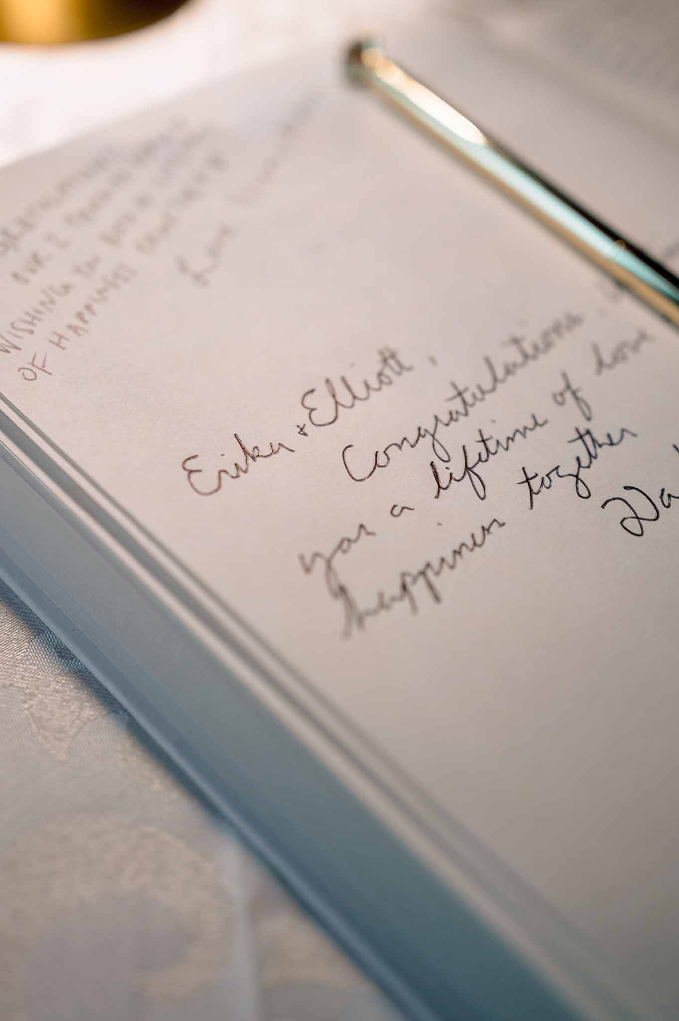 Open wedding guest book with handwritten message and silver pen on white linen surface