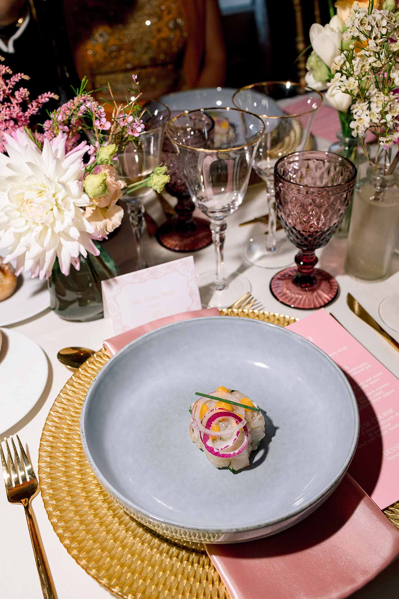 Plated starter on blue ceramic plate with gold charger blush napkin and dahlia centerpiece