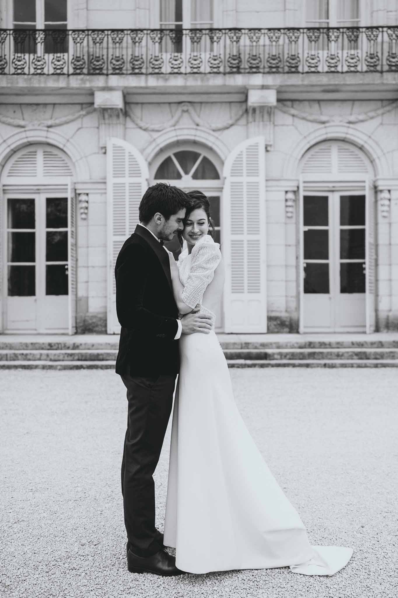 Bride and groom embracing with Chateau d'Arcelot visible in the background