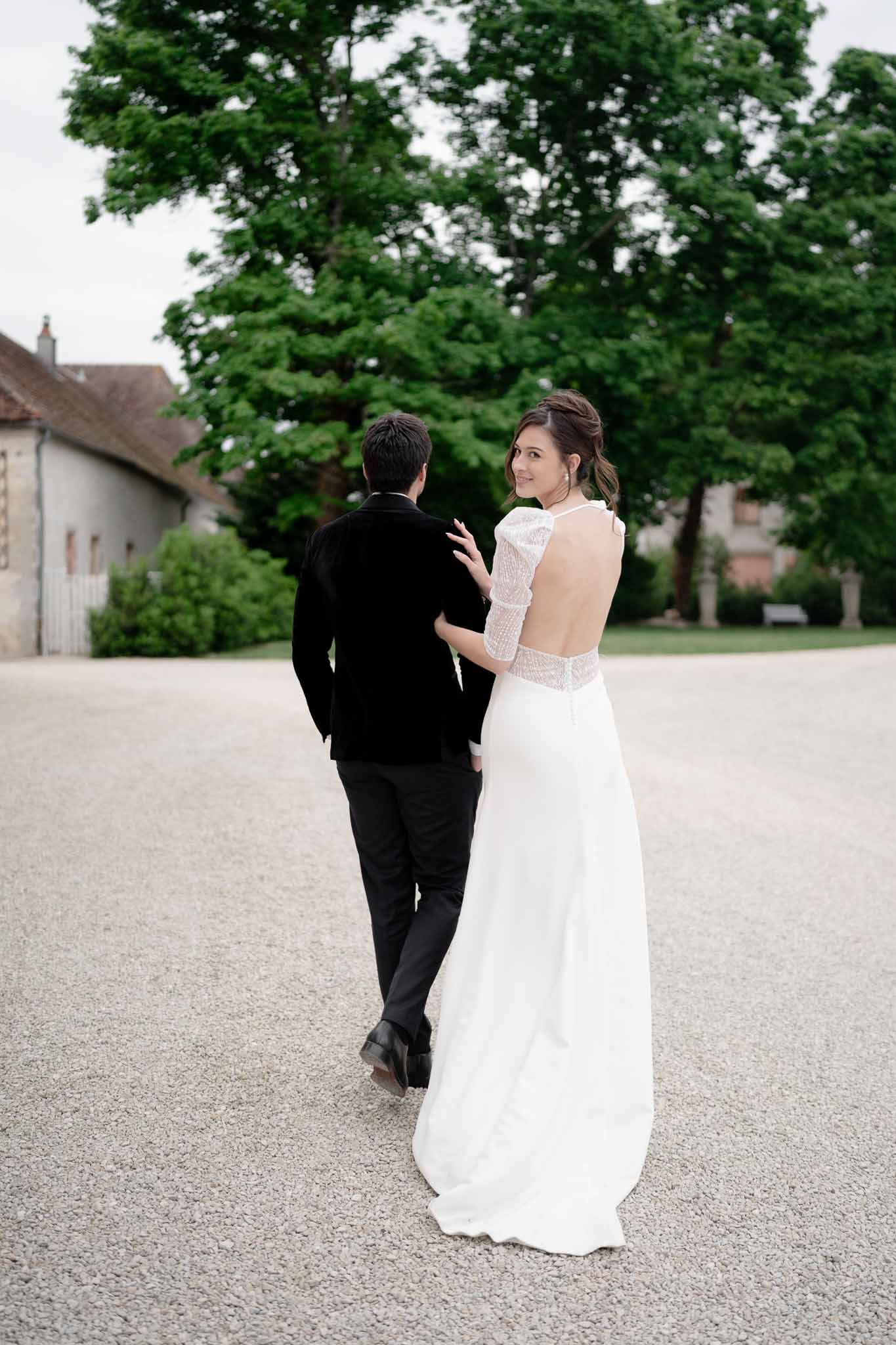 Bride and groom walking together through the chateau gardens, bride's open-back dress visible