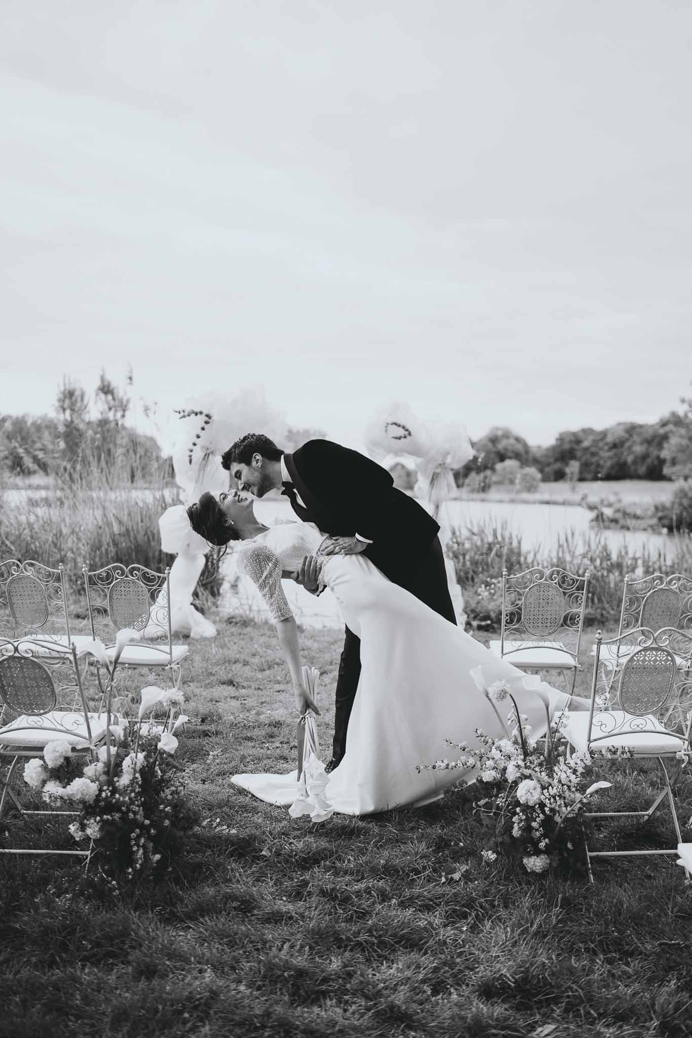 Groom dips bride for a kiss at the lakeside ceremony with floral arch behind