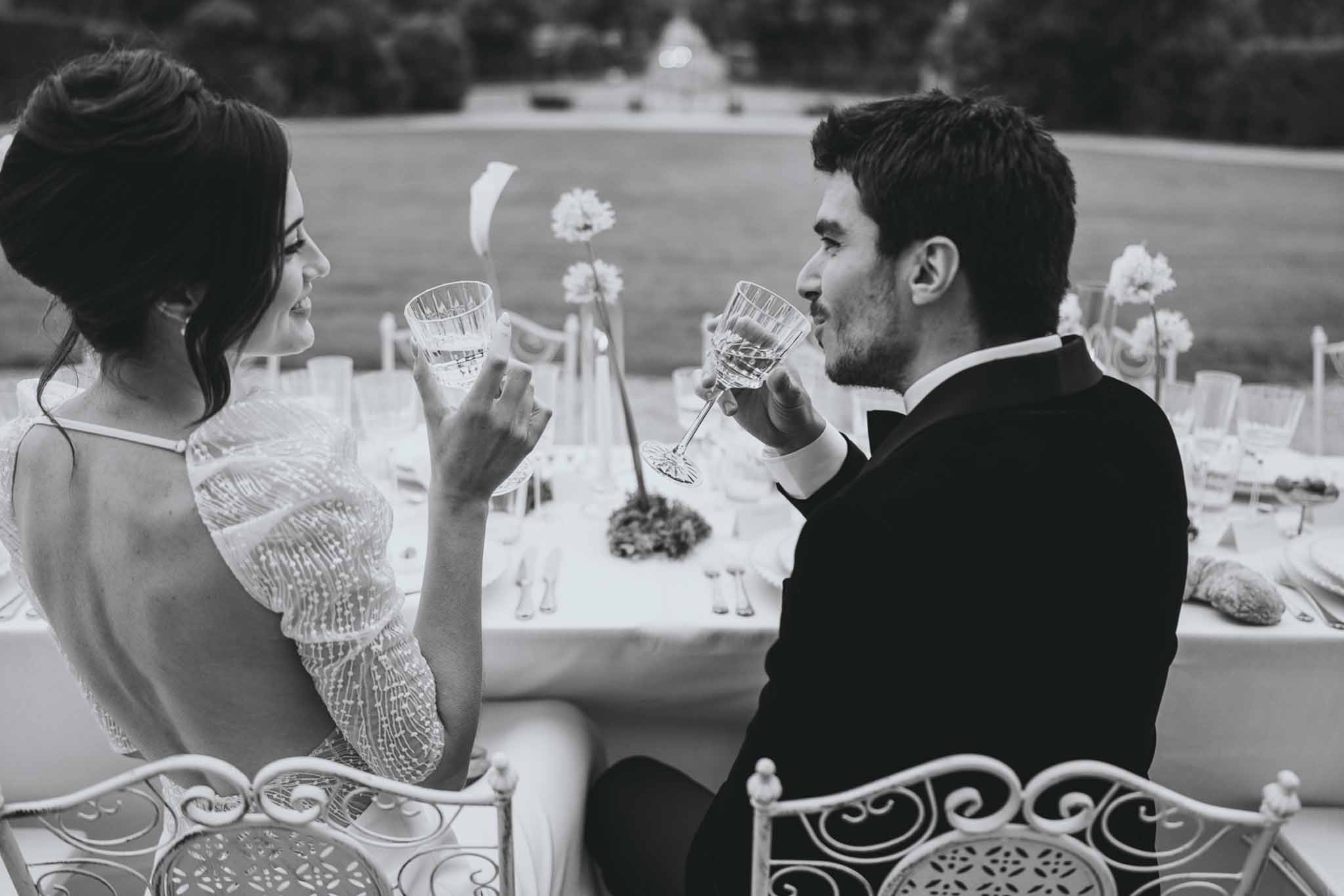 Couple seated at reception table sharing a champagne toast