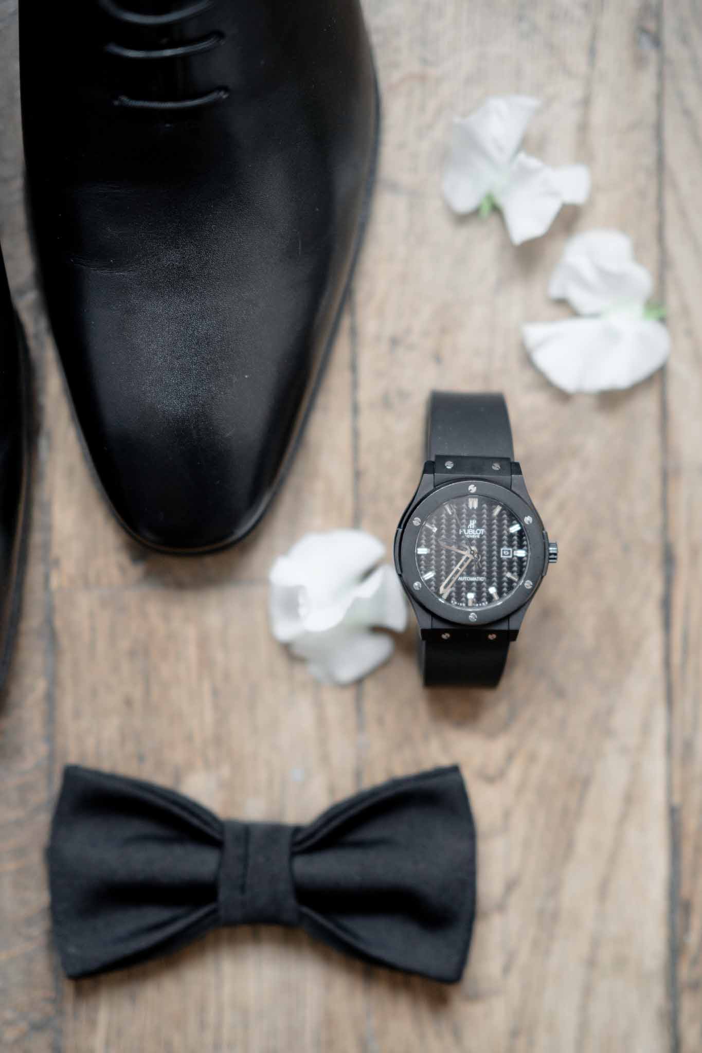 Flatlay of groom's black dress shoes and accessories