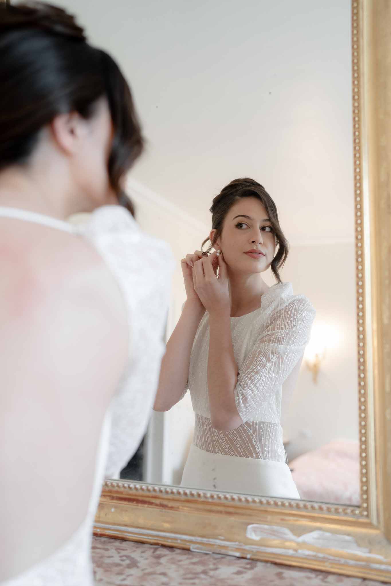 Bride reflected in mirror as she puts on earrings during getting ready