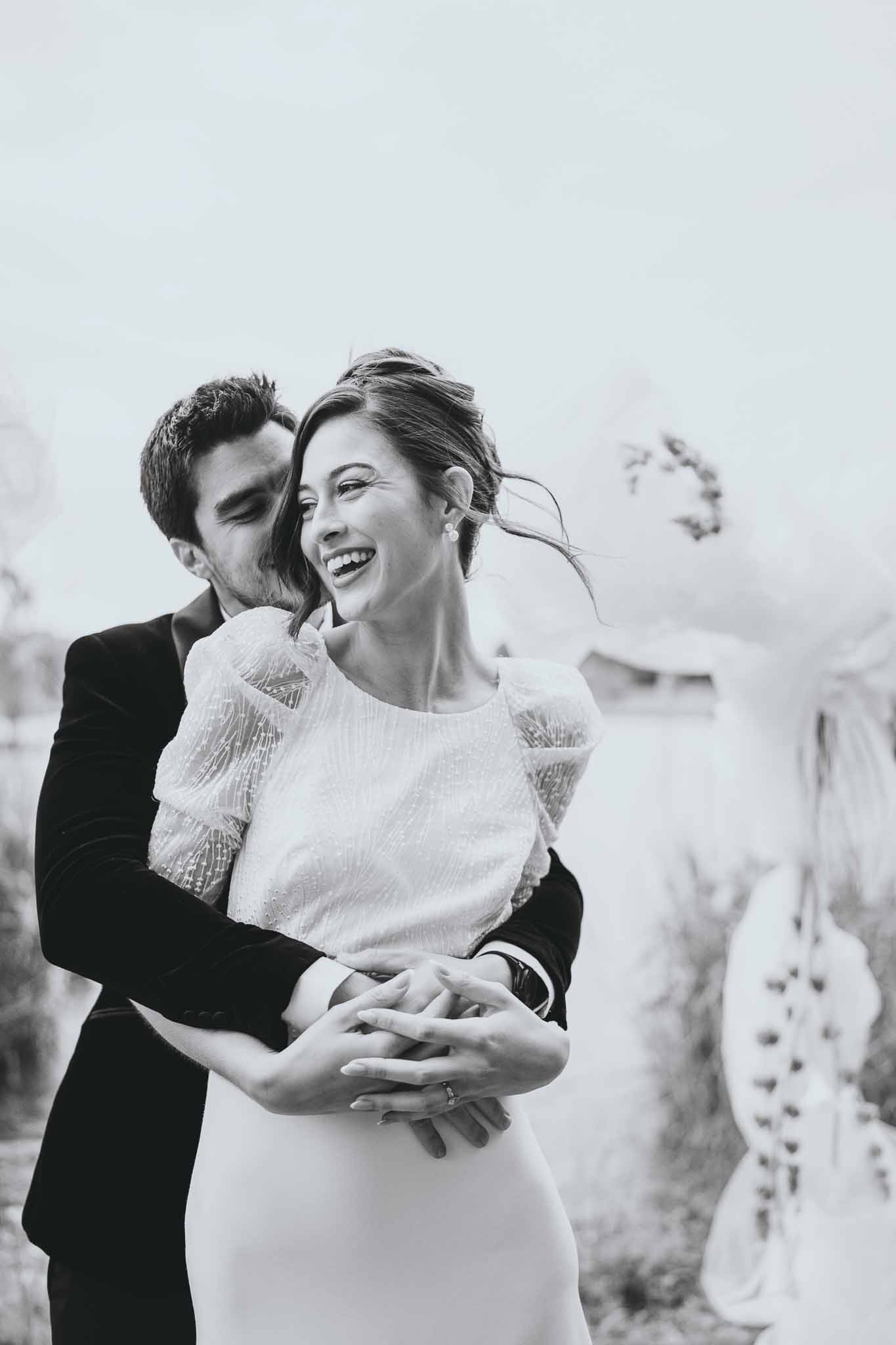 Groom wraps arms around bride from behind at the ceremony altar
