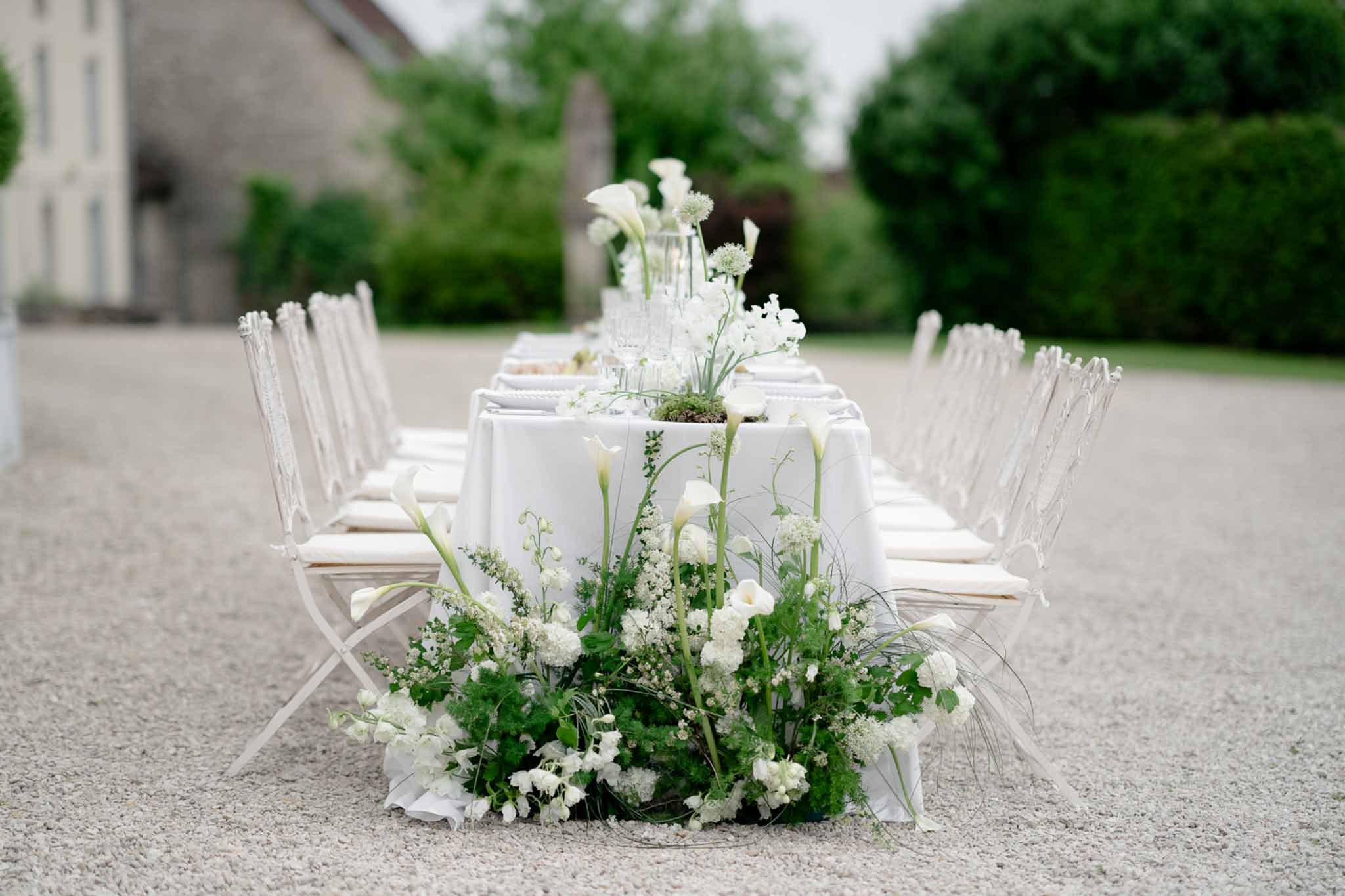 Long reception table viewed from end with floral centerpieces and garden backdrop