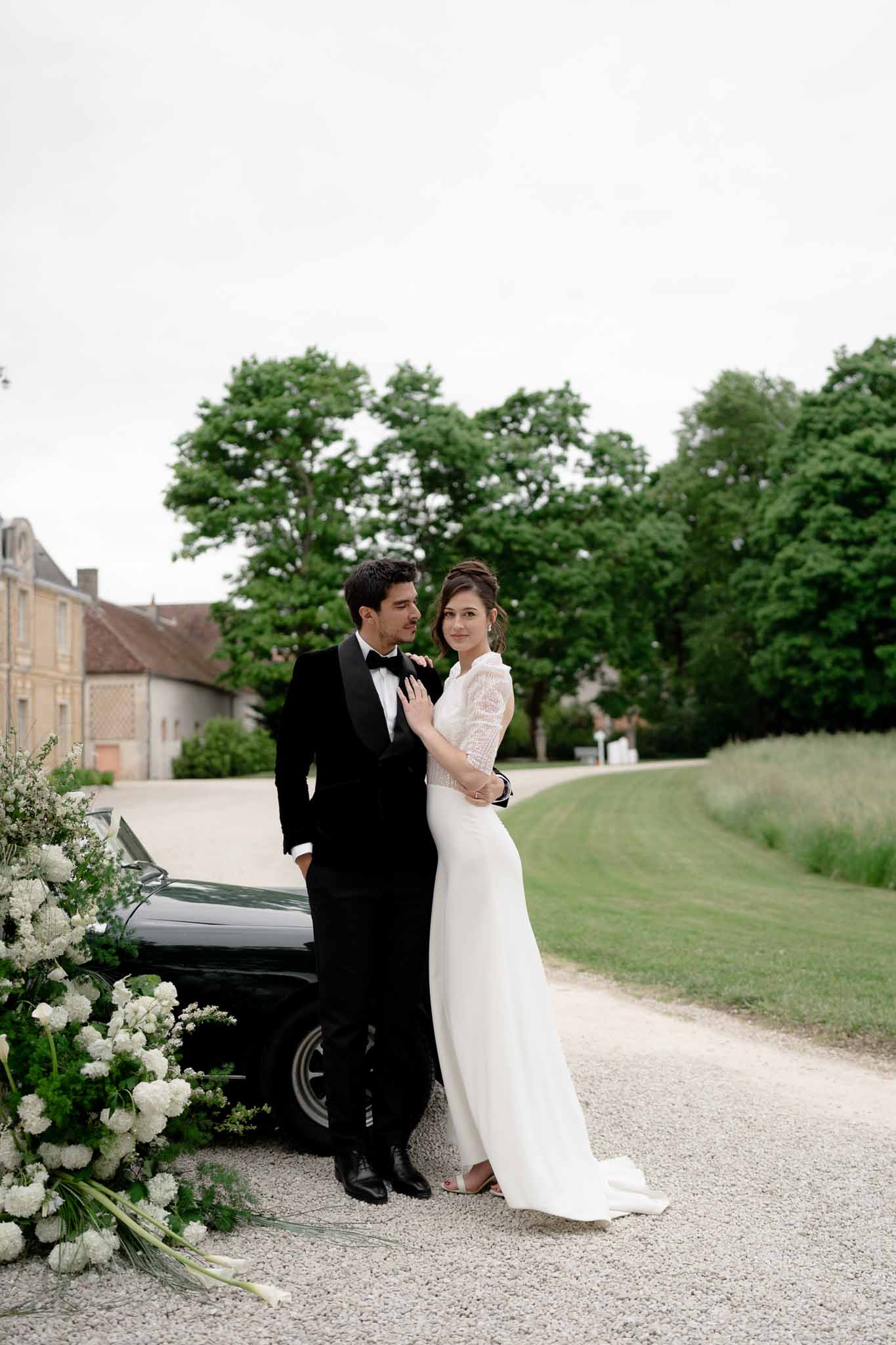 Couple embracing while leaning on the hood of the black vintage car