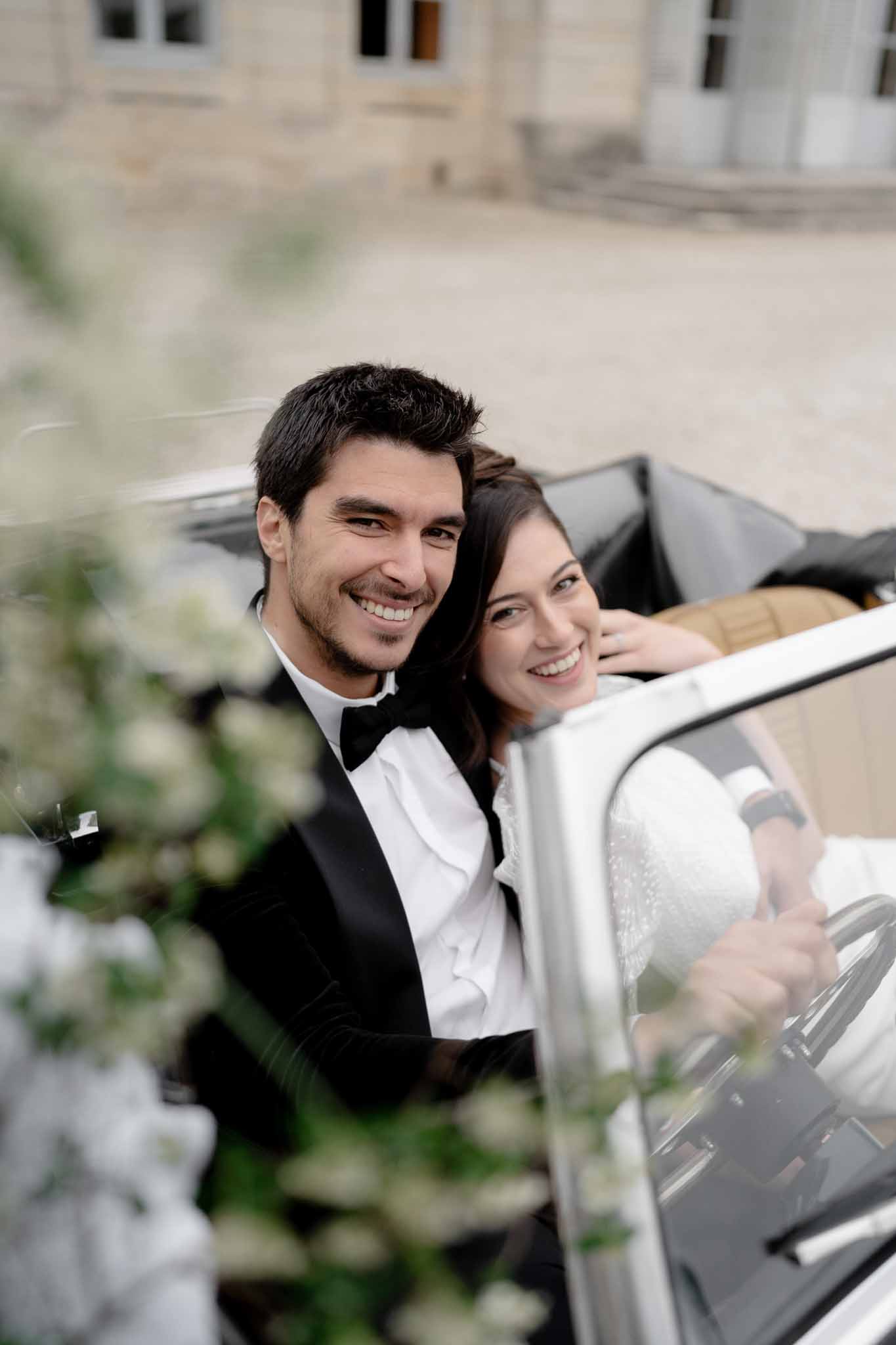 Couple hugging beside the black vintage car at Chateau d'Arcelot