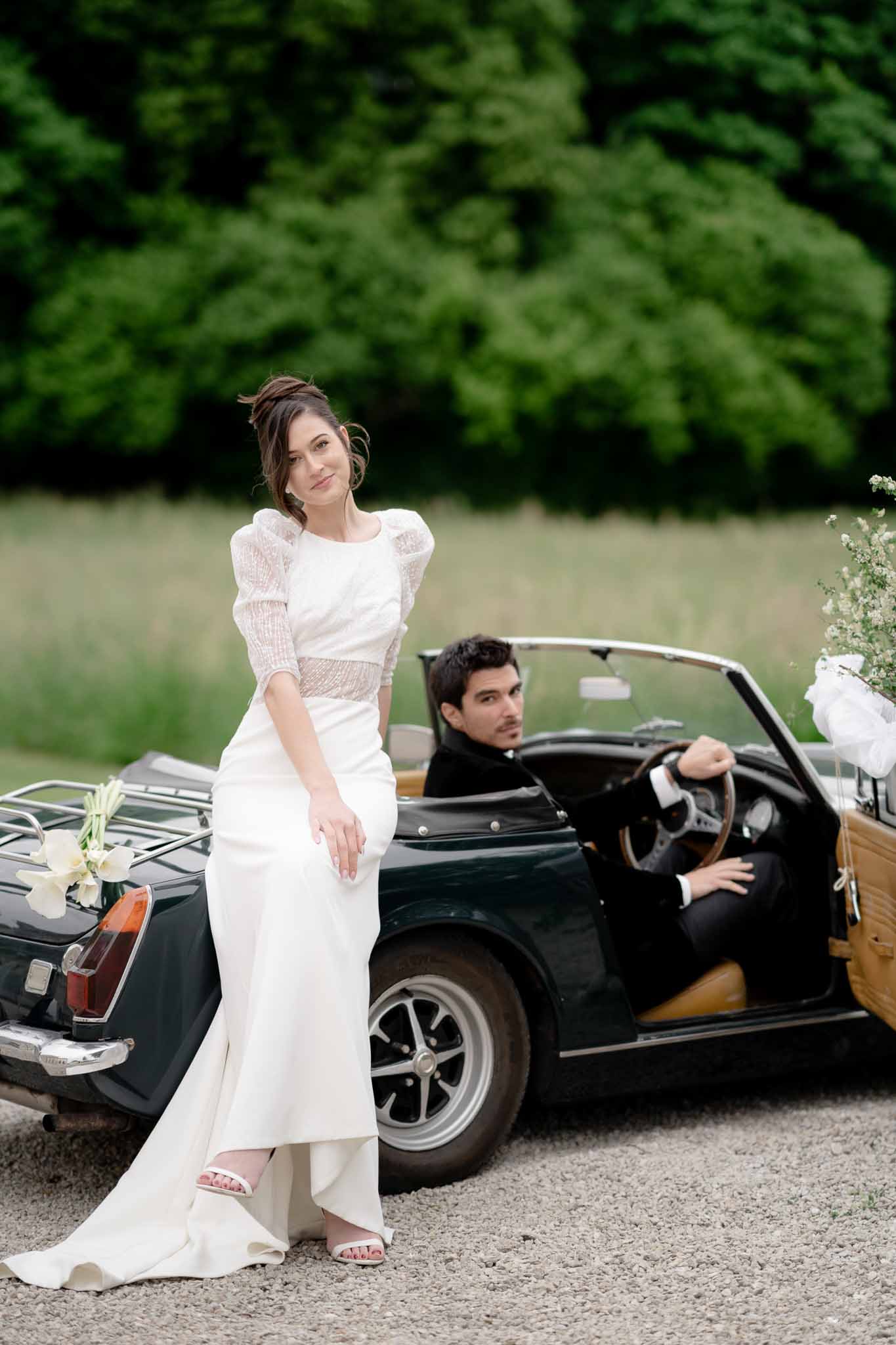 Groom seated inside vintage car looking at bride who stands outside