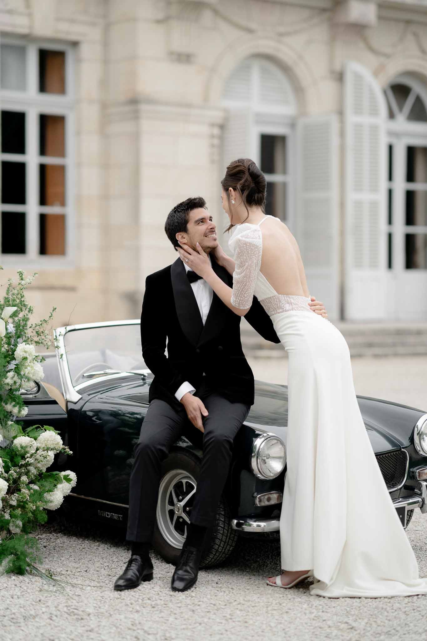 Groom sits in vintage car while bride stands elegantly beside it