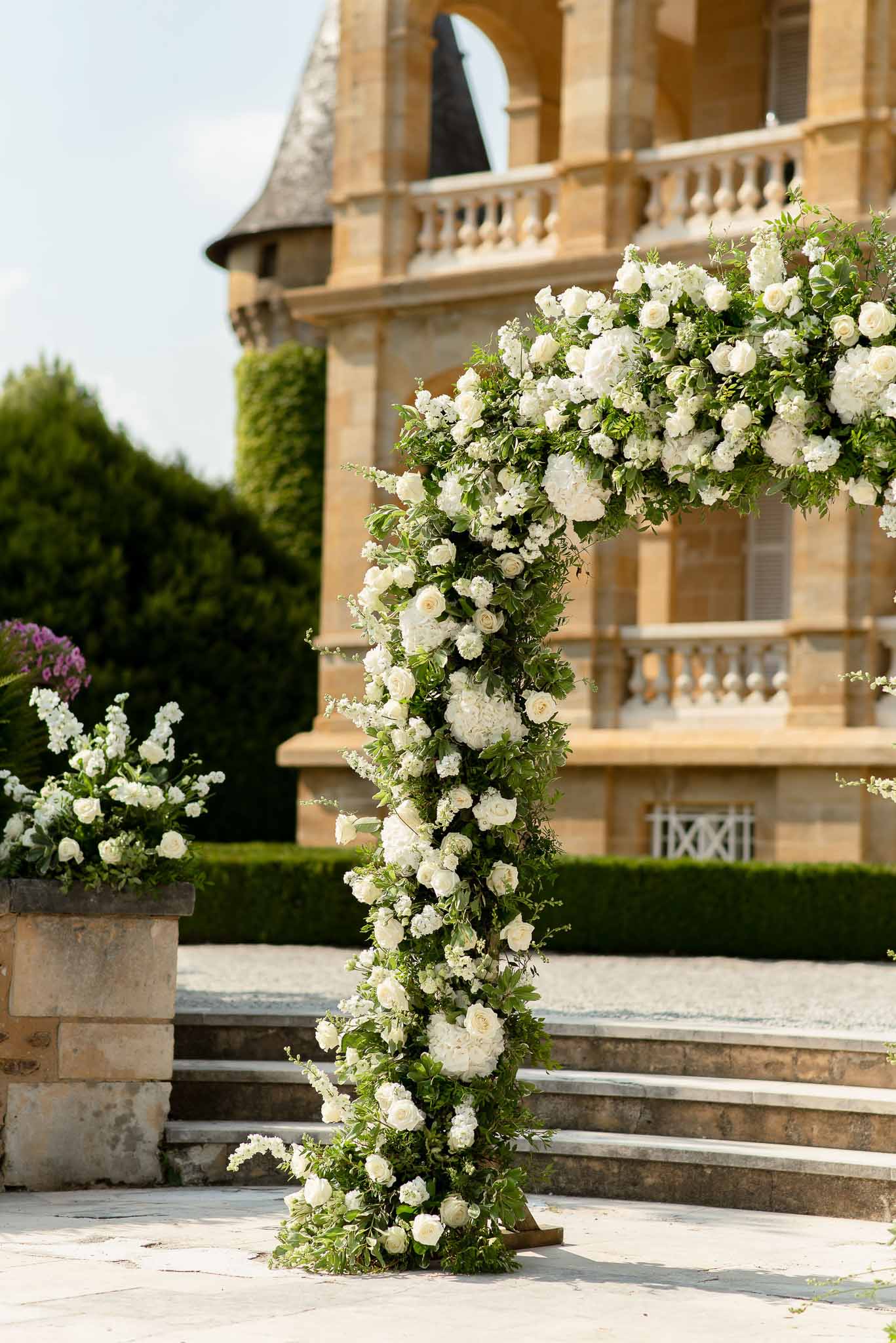 Tall white rose and hydrangea ceremony column with cloud arrangement before chateau tower and balustrade