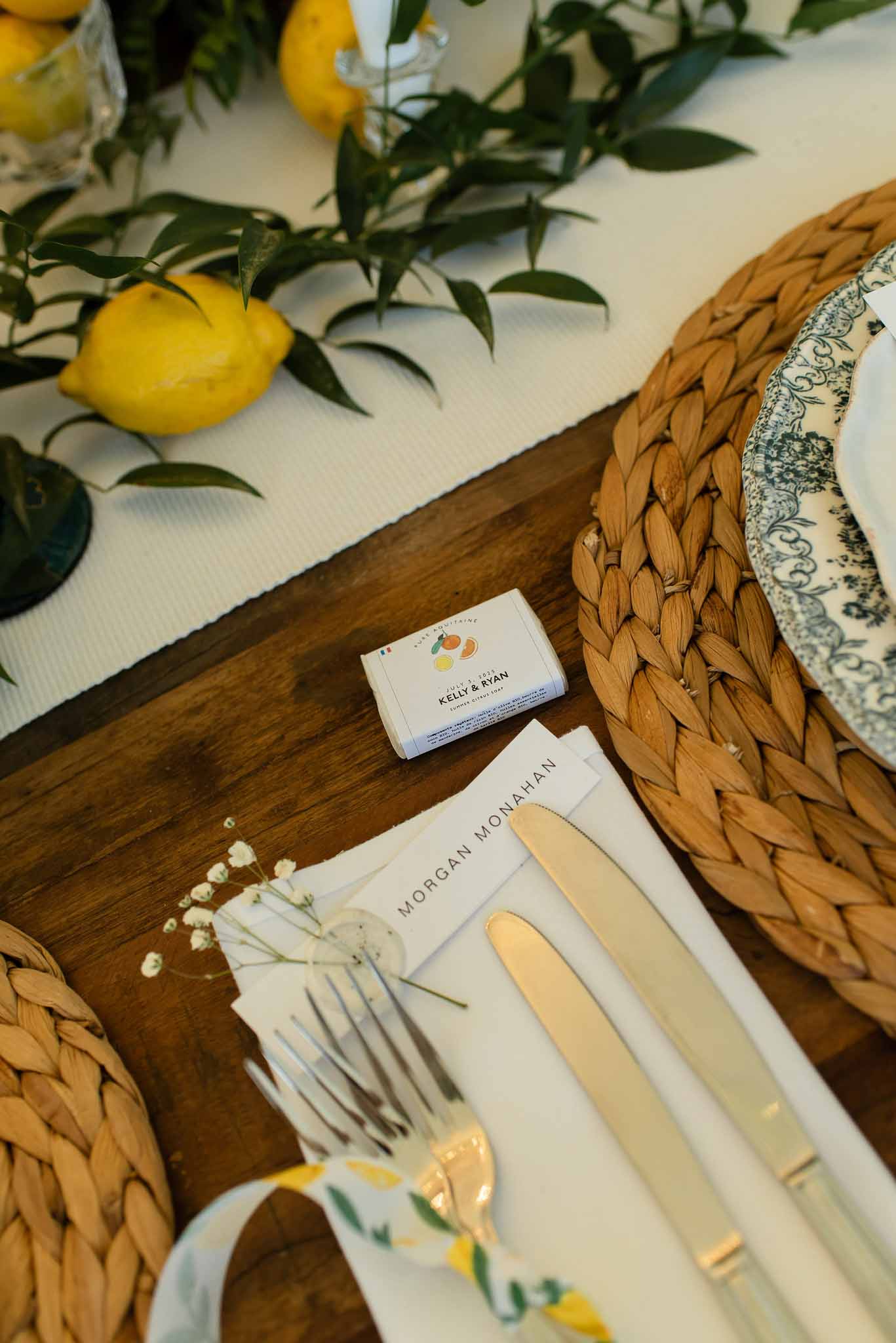 Citrus-themed place setting with toile plates seagrass placemat lemon-print ribbon gold flatware and personalized soap favor