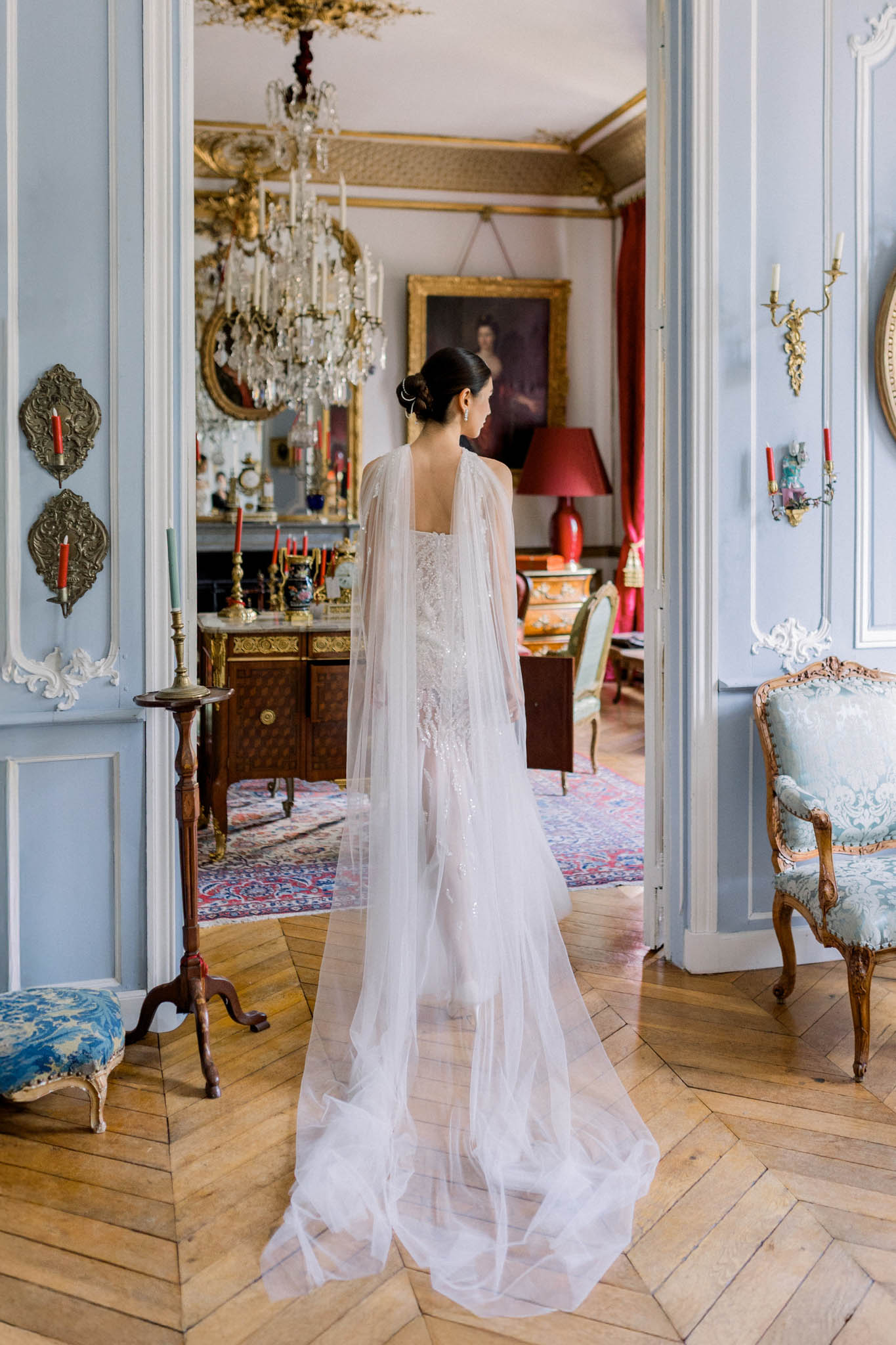 Bride from behind in ivory lace gown with tulle cape in powder blue chateau salon with gilded mouldings