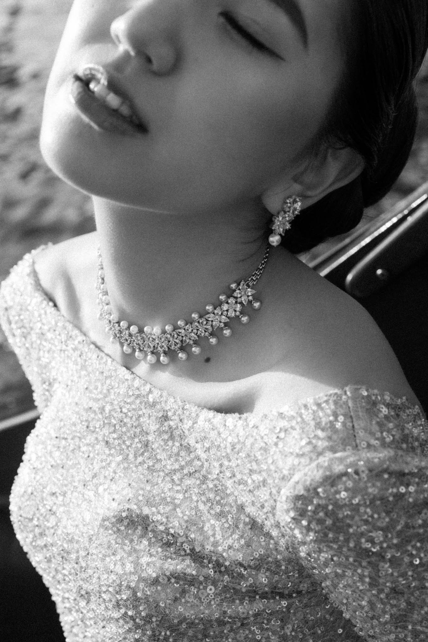 Black and white close-up of bride's pearl and crystal floral necklace and sequined off-shoulder bodice