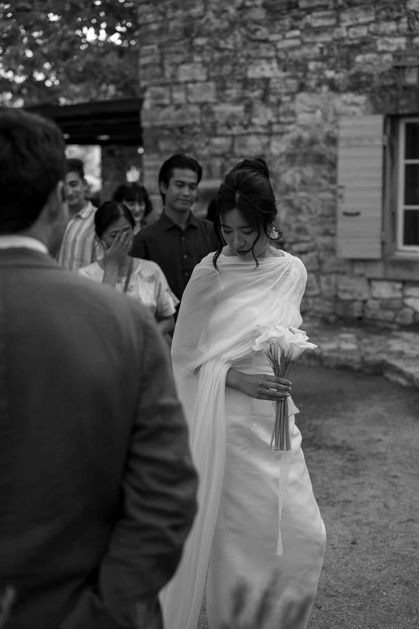 Bride in elegant gown with cape holding calla lily bouquet during outdoor ceremony