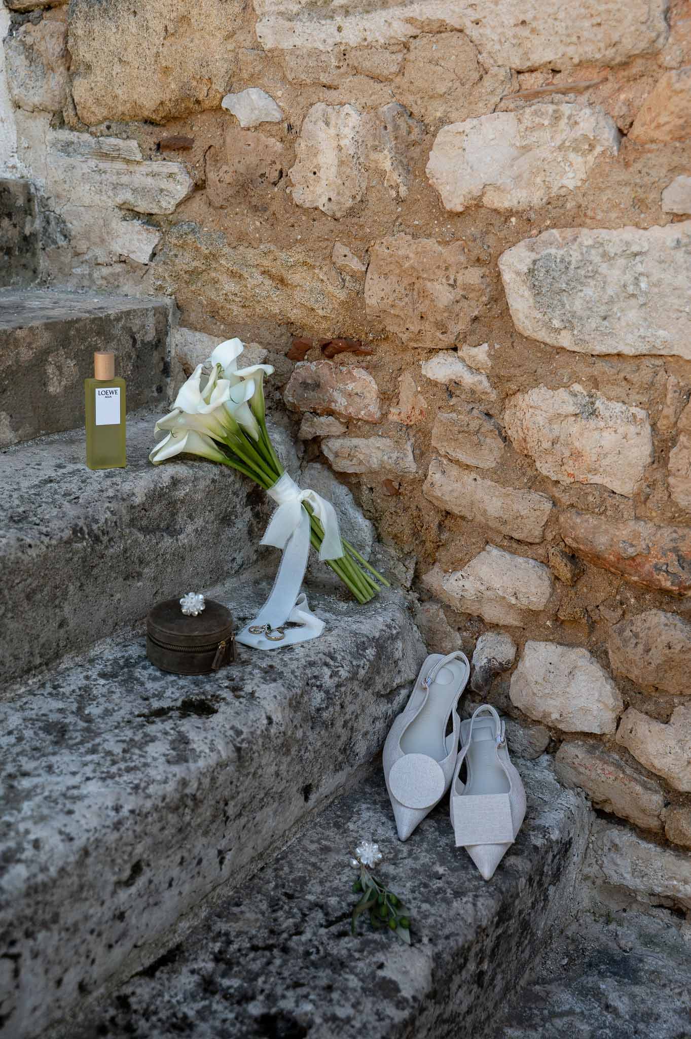 Bridal flat lay detail: calla lily bouquet, white shoes and accessories on stone stairs