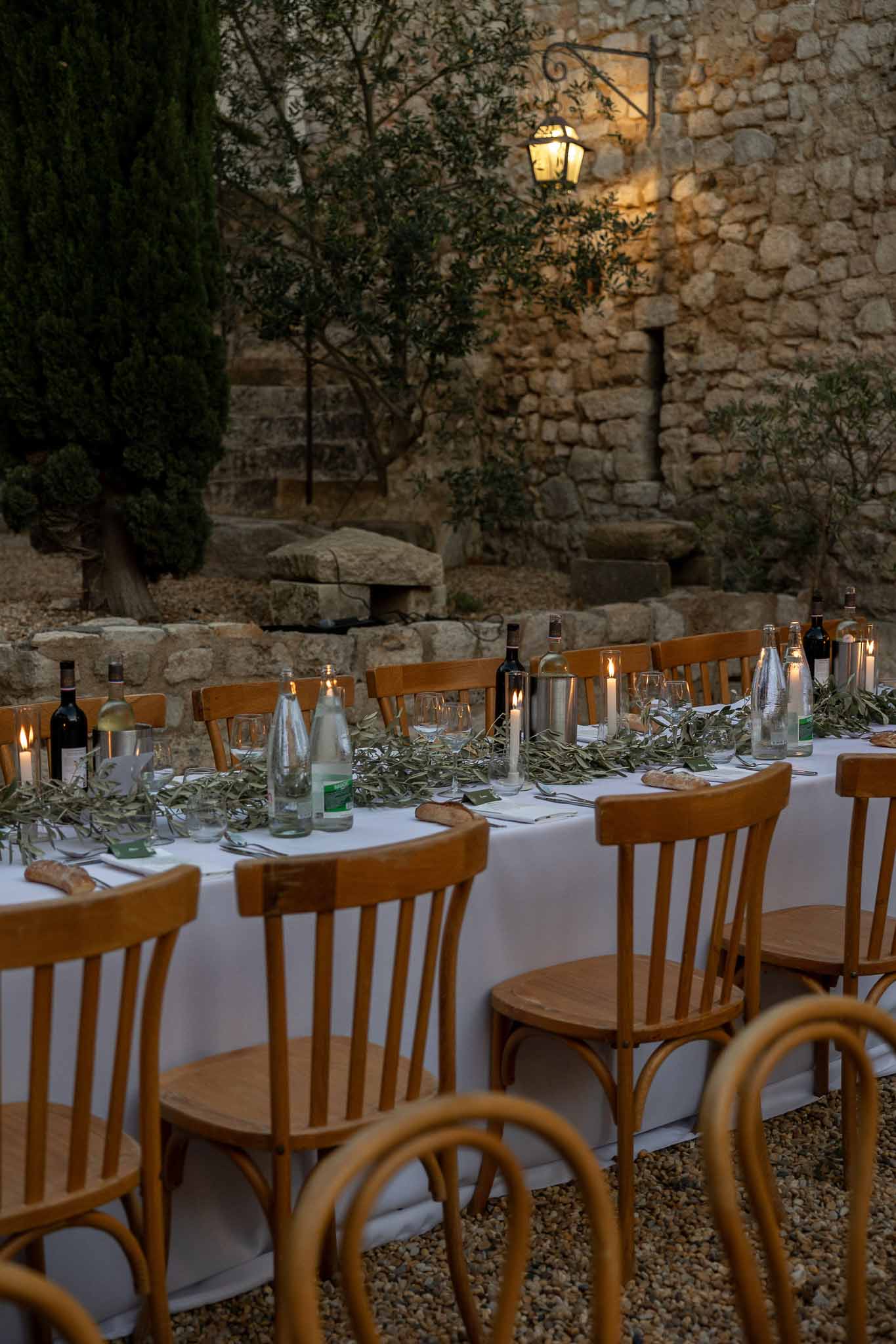 Glass vase centrepieces with candles and wooden cross-back chairs at outdoor reception