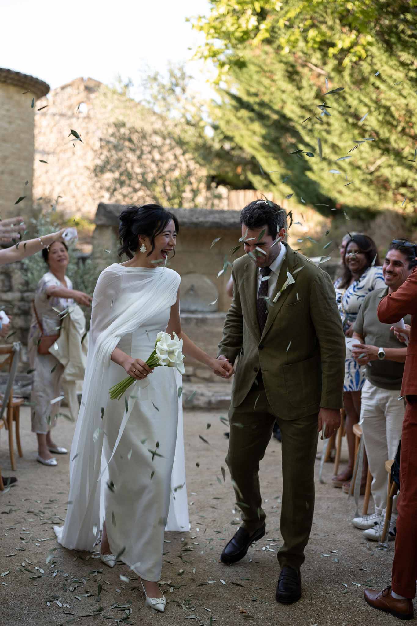 Guests tossing olive leaves as couple walks along ceremony aisle at Notre-Dame de Conil