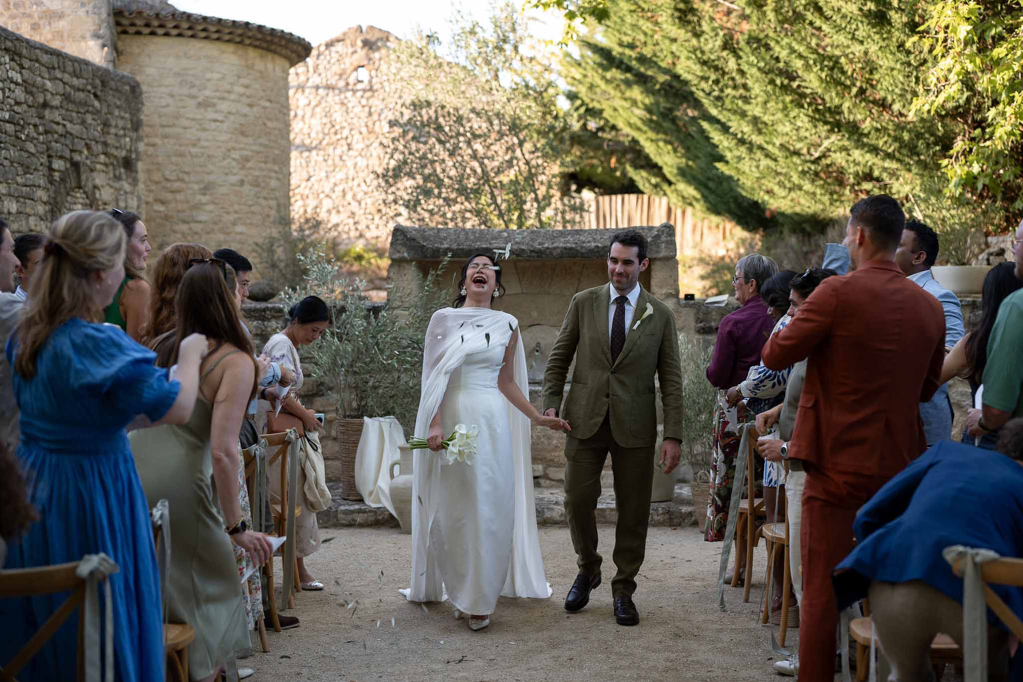 Guests showering couple with petals as they walk down ceremony aisle