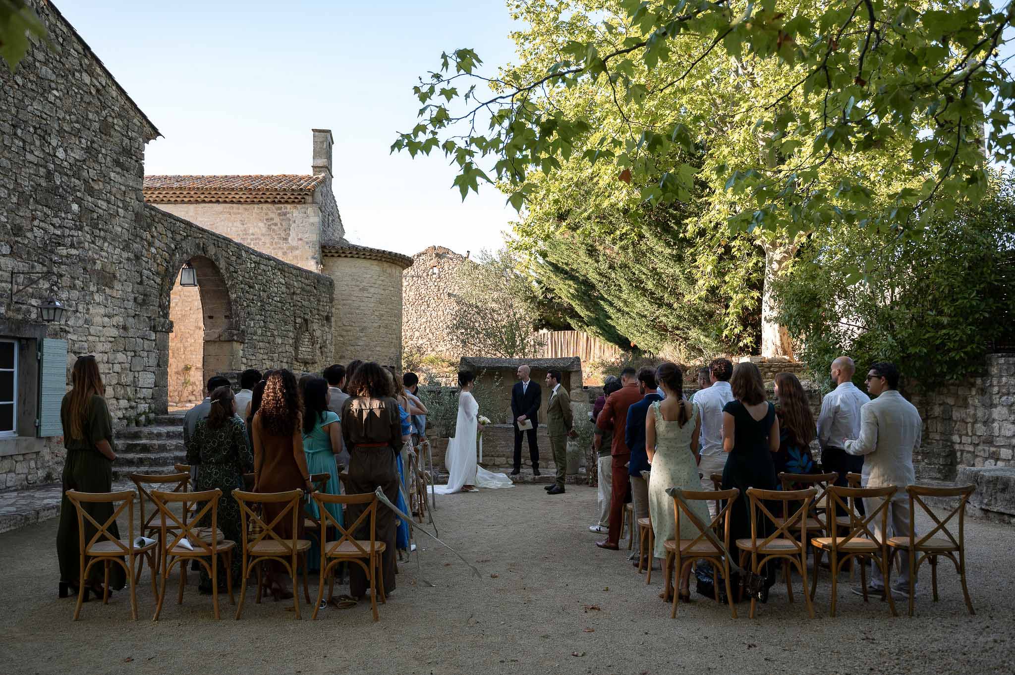 Couple seated at altar with officiant and wooden chair rows of guests at Notre-Dame de Conil