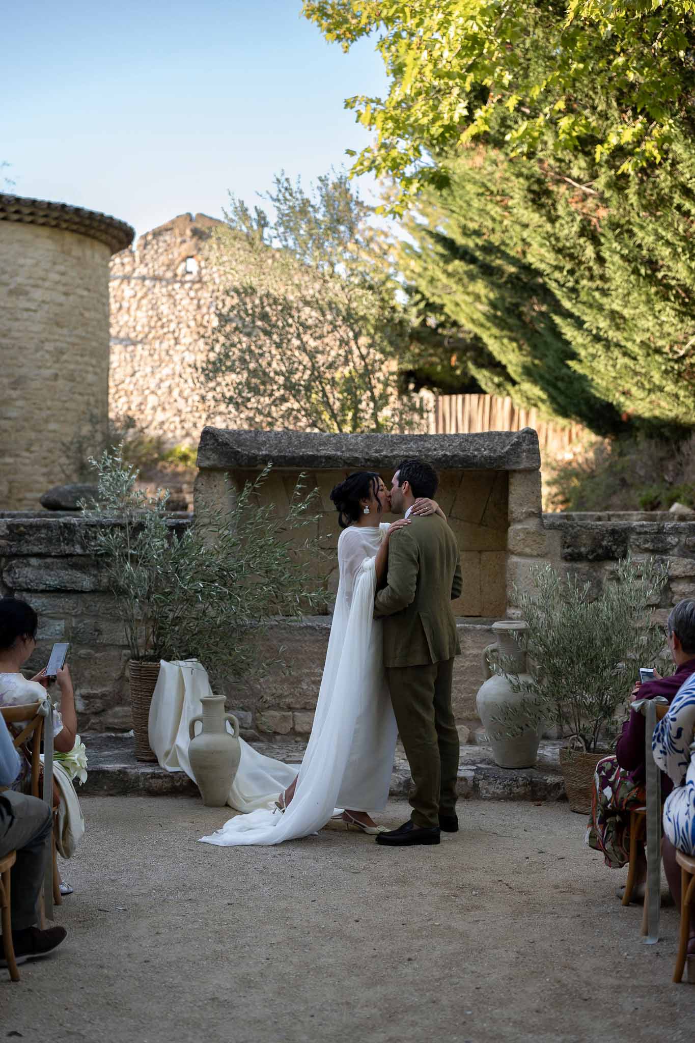 Couple sharing first kiss under olive branch arch altar at outdoor ceremony
