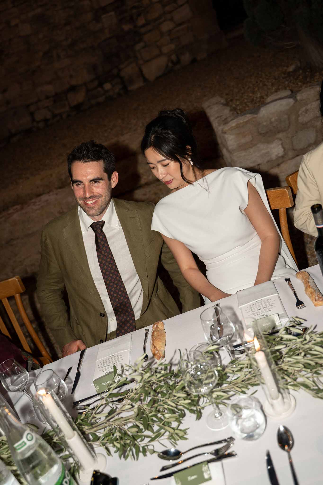 Bride and groom seated together at head of reception dinner table in garden