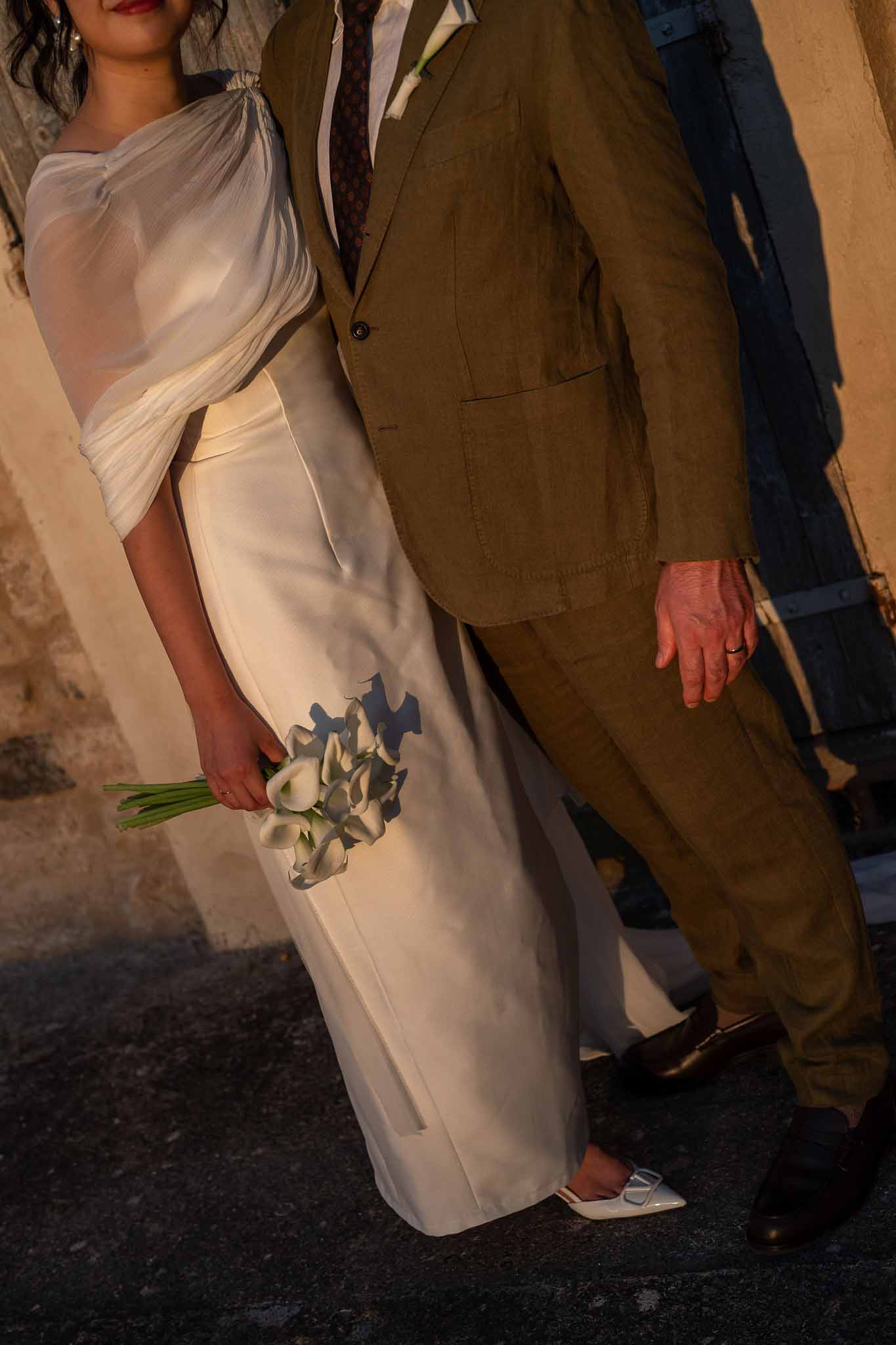 Bride holding calla lily bouquet with dress detail in warm golden evening light