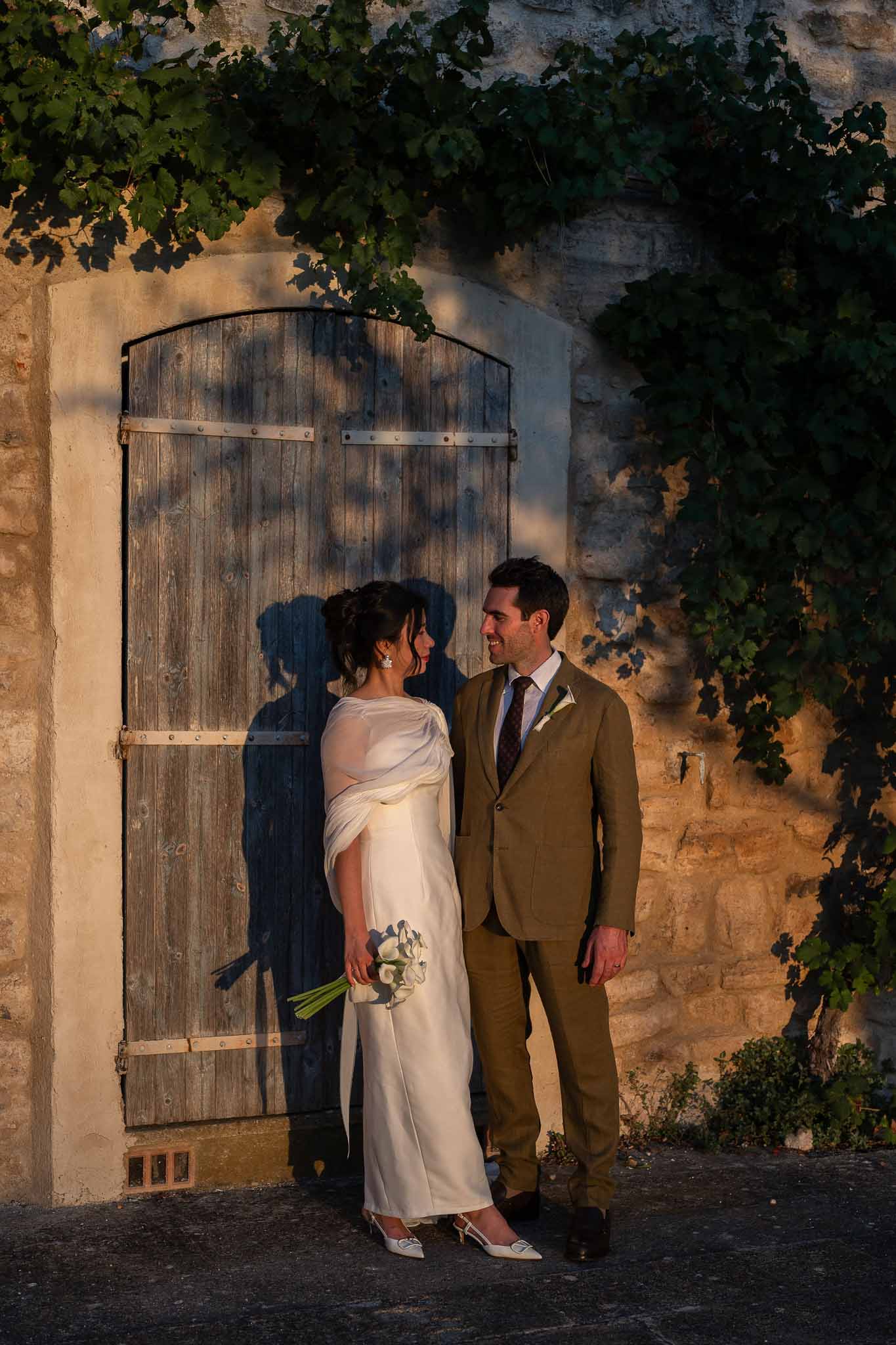 Couple standing together at vintage wooden door surrounded by garden greenery in golden hour