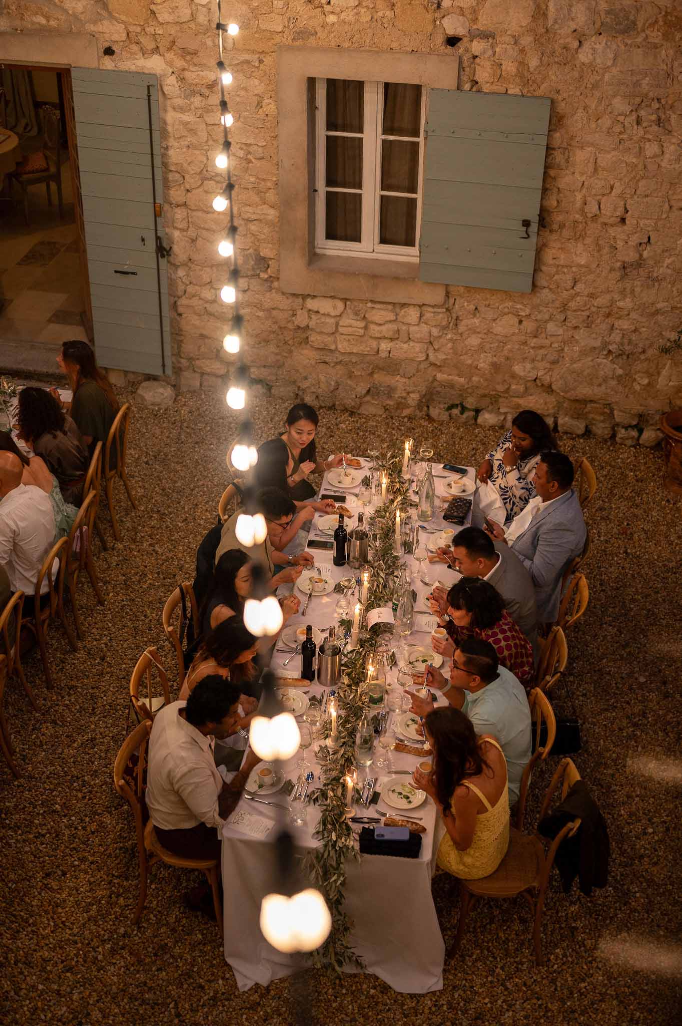 Top-down aerial view of reception dinner table set with olive branch centrepieces and guests seated