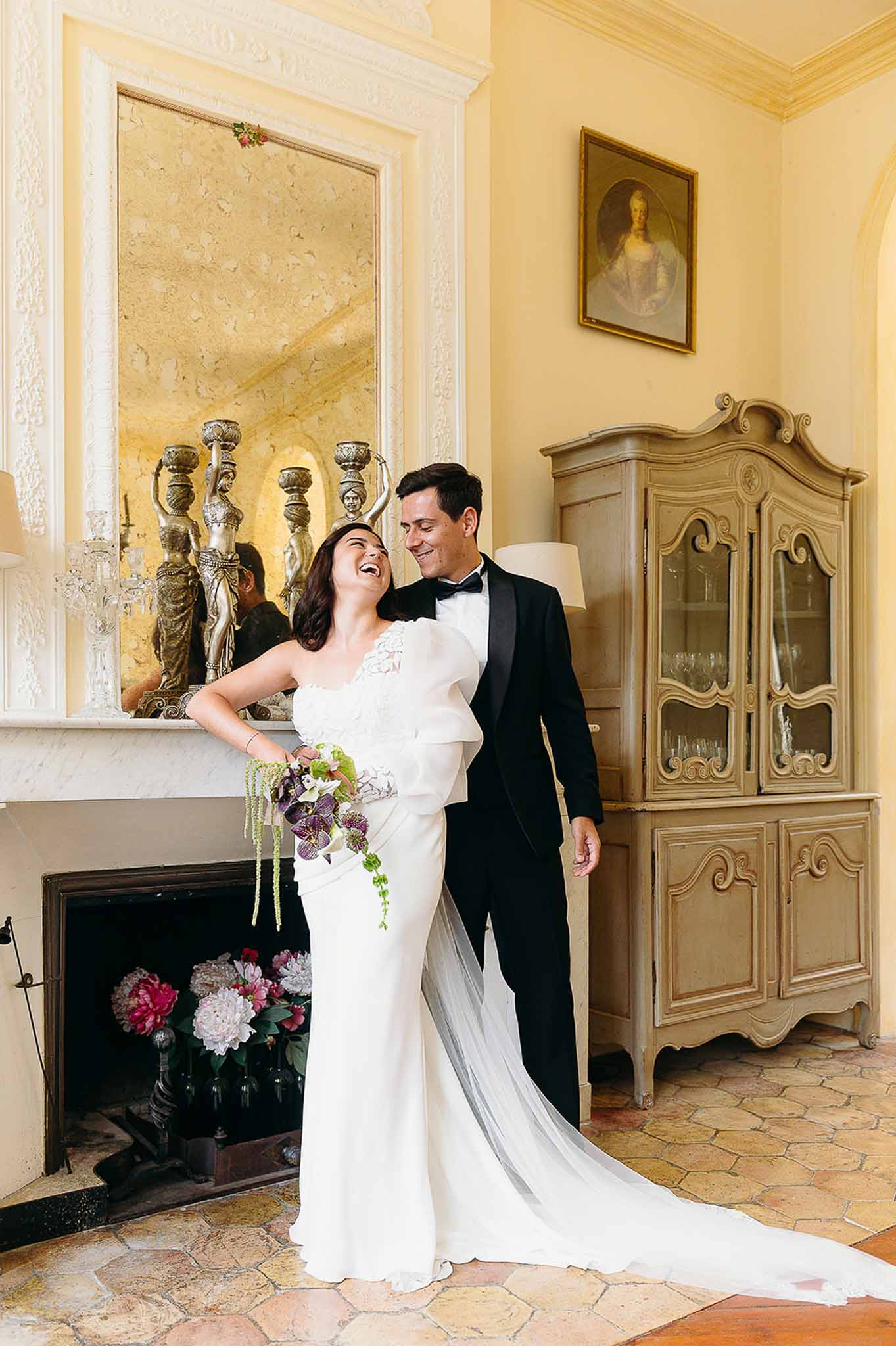 Bride holding bouquet while couple poses by a vintage chimney at Domaine de Perrotin