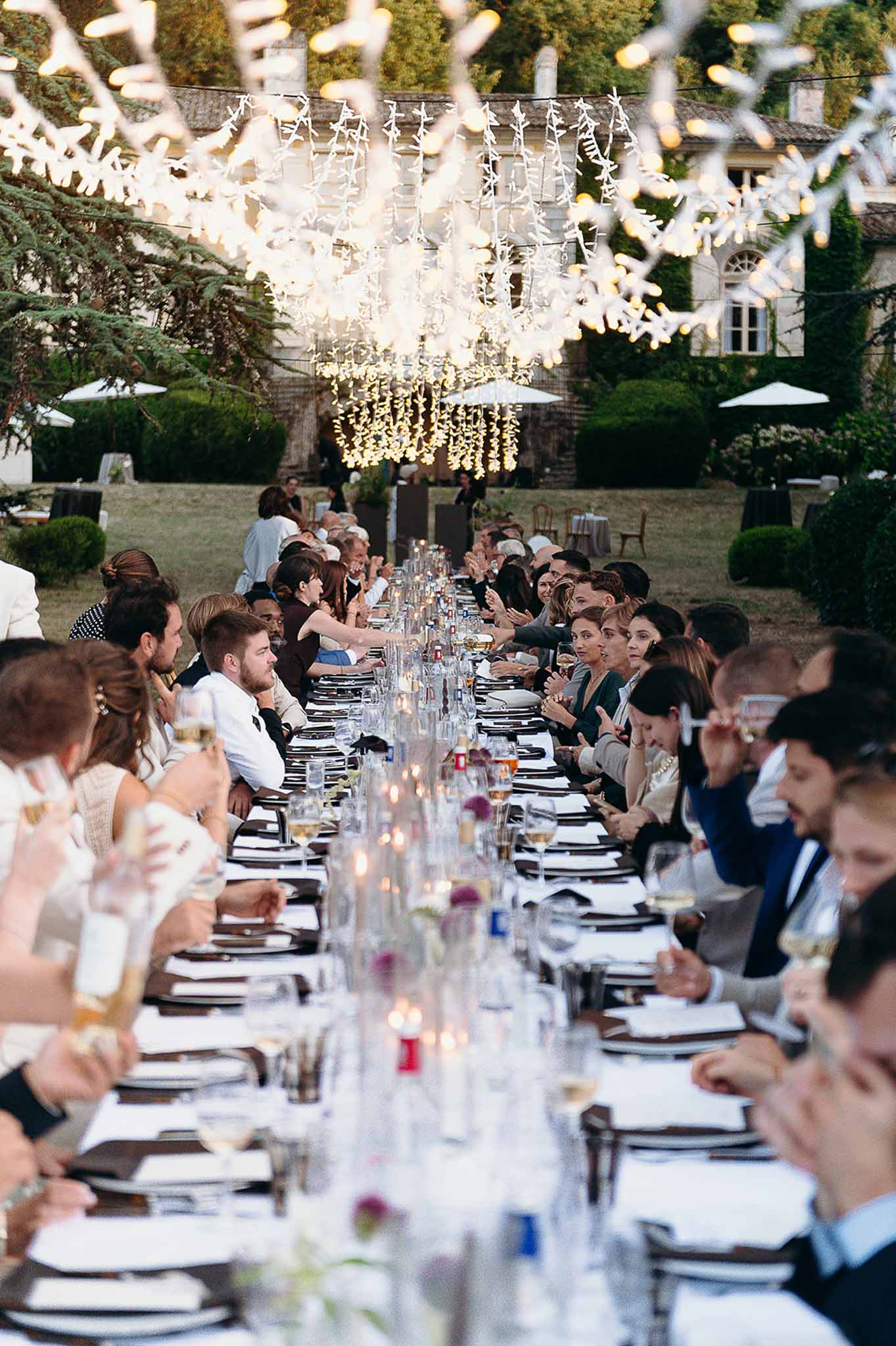 Reception centrepiece of candles and glasses with string lights and seated guests at Domaine de Perrotin