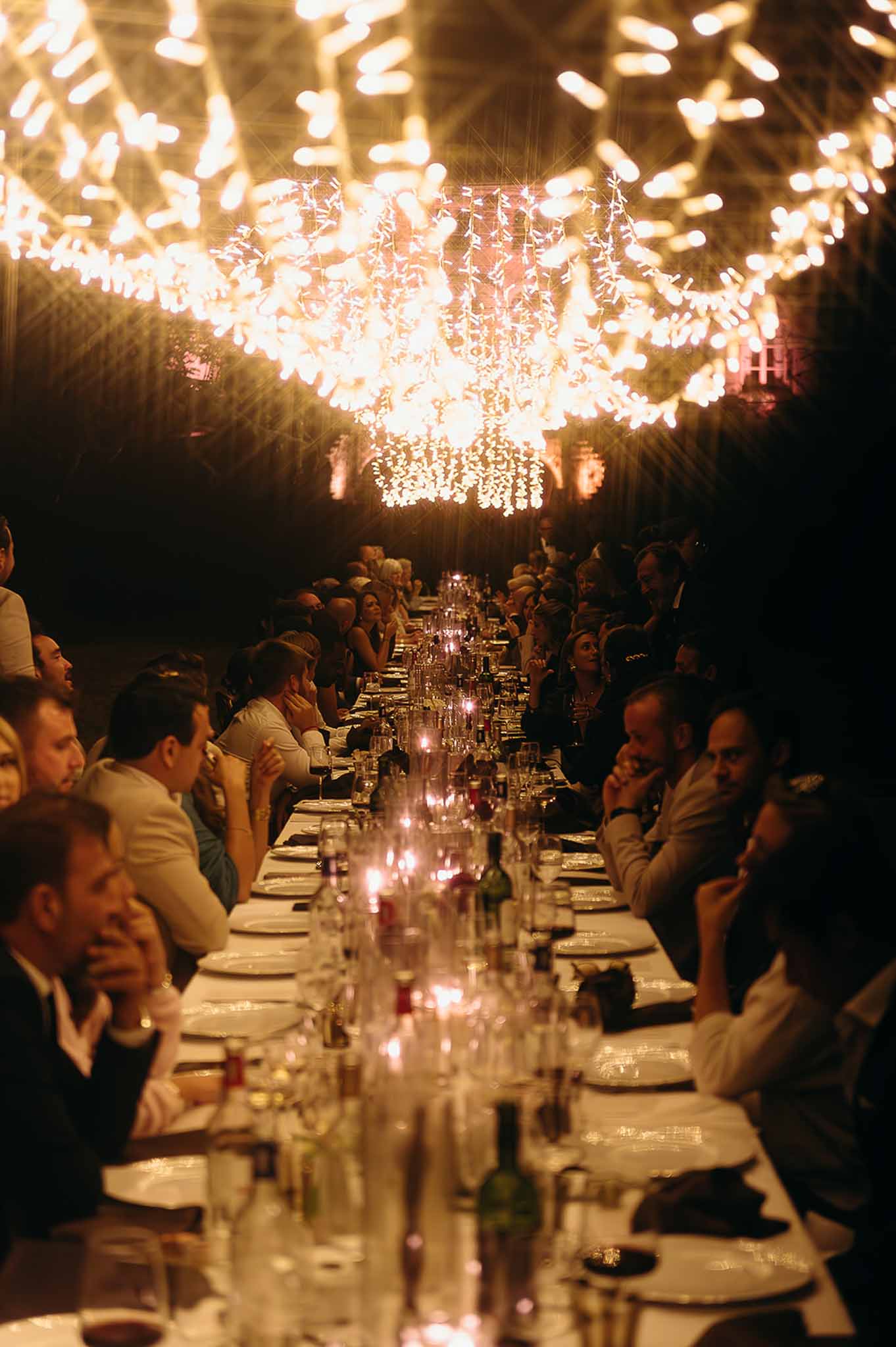 Long reception table with floral centrepiece and candles surrounded by guests at Domaine de Perrotin