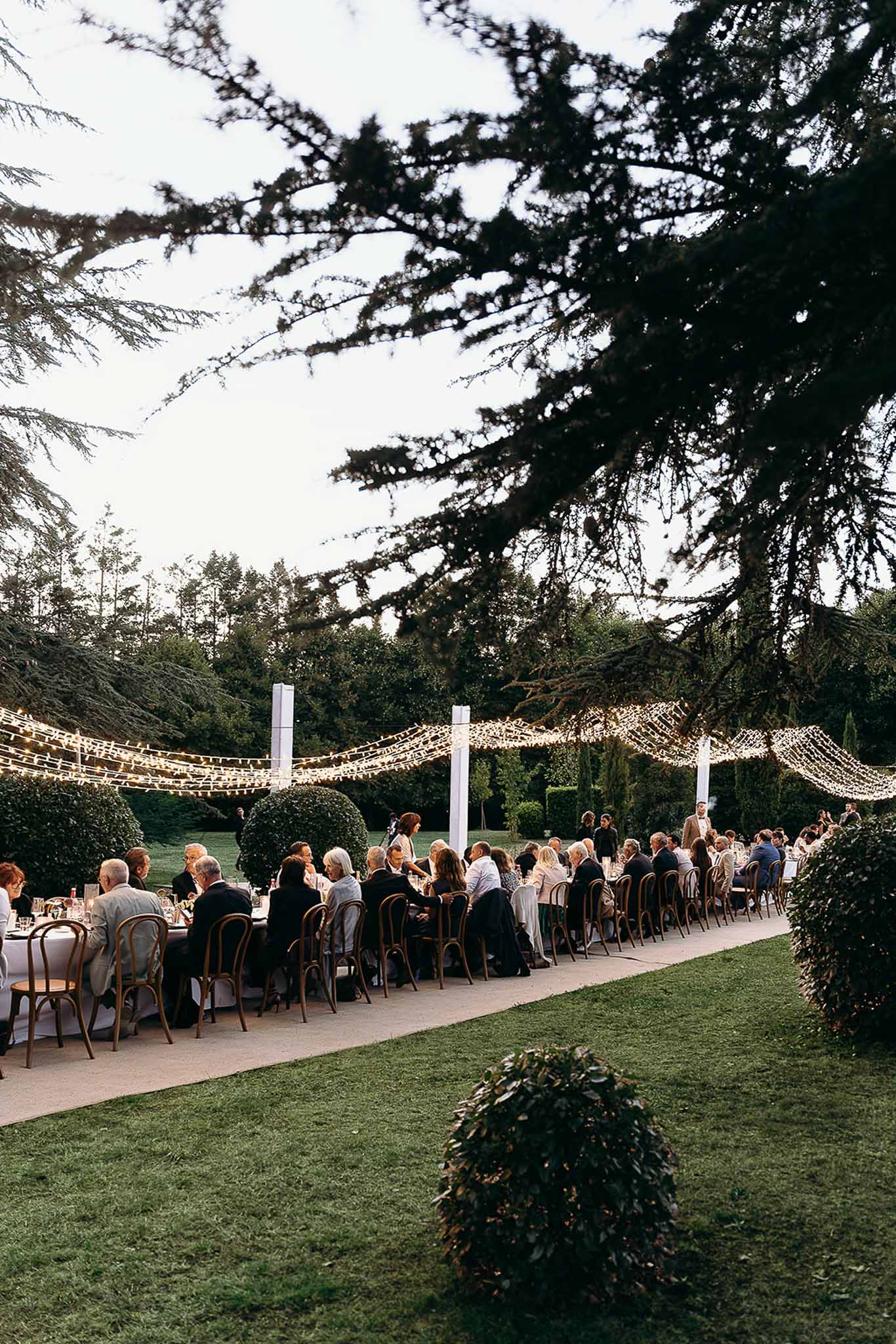 Long reception table with string lights and seated guests in the garden at Domaine de Perrotin