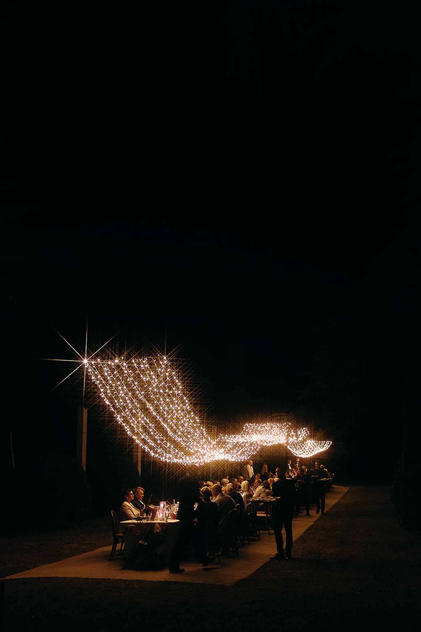 String lights illuminating the dinner tables and guests at the reception at Domaine de Perrotin