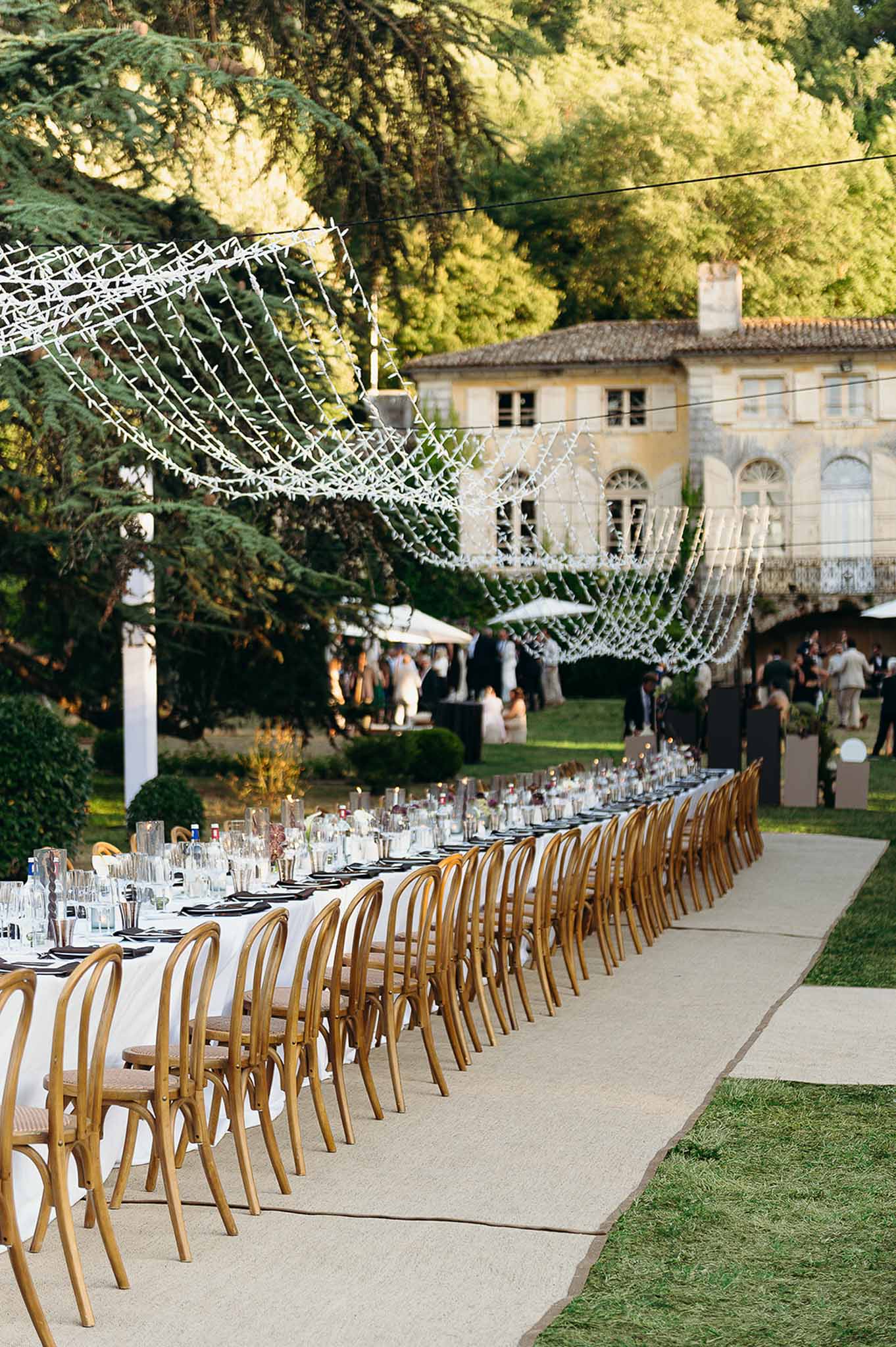 Long reception tablescape with wood chairs and string lights at Domaine de Perrotin