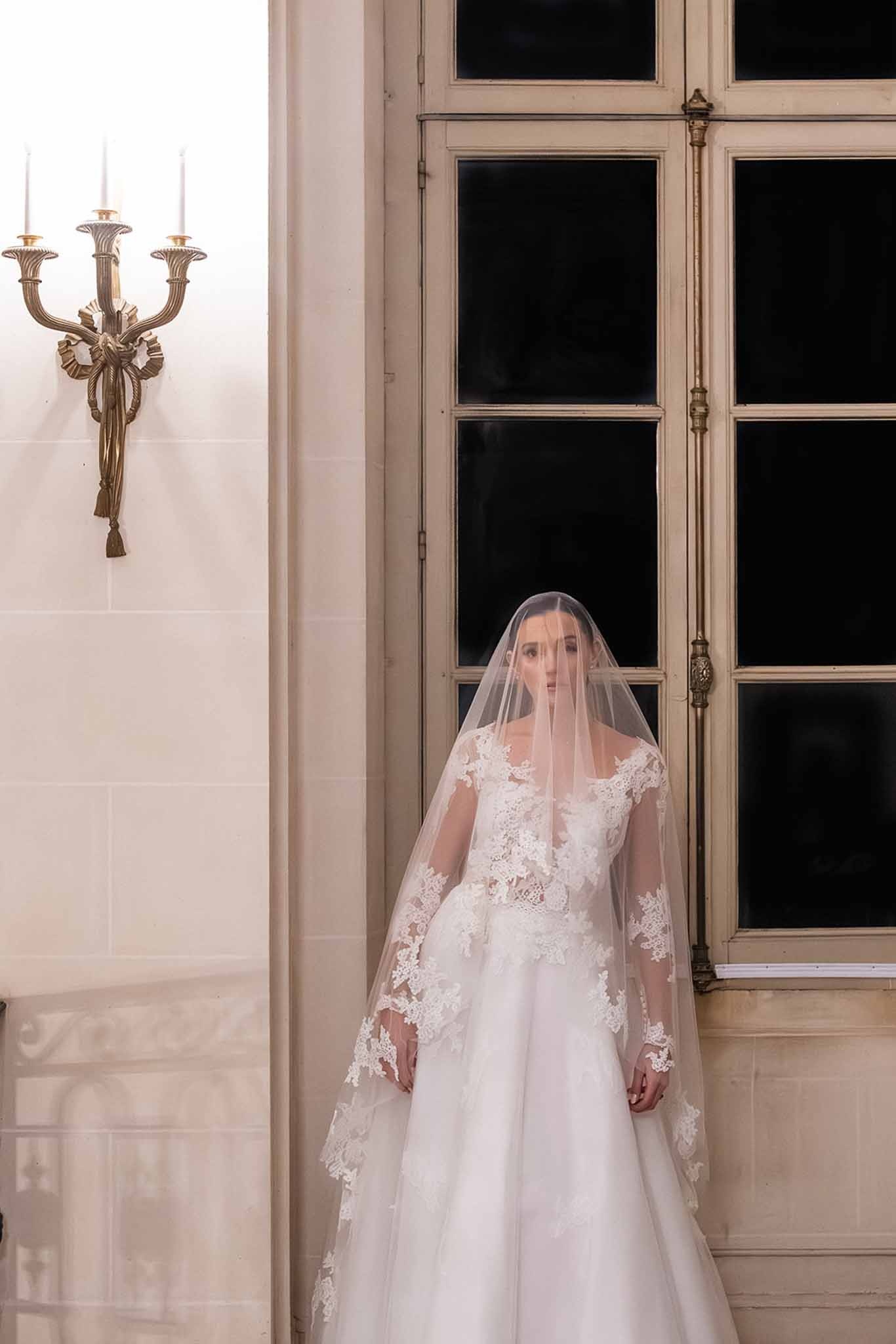 Bride in lace gown with cathedral veil at Chateau du Terral window