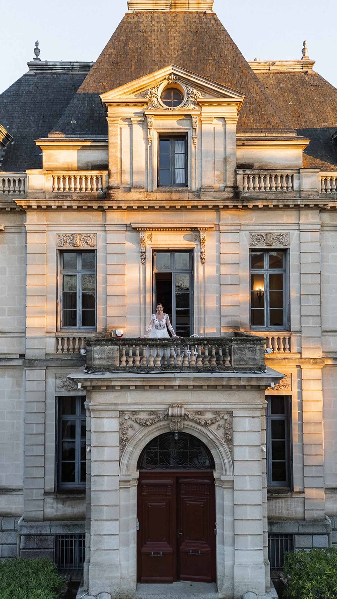 Bride on balcony at golden hour showing full Chateau du Terral facade