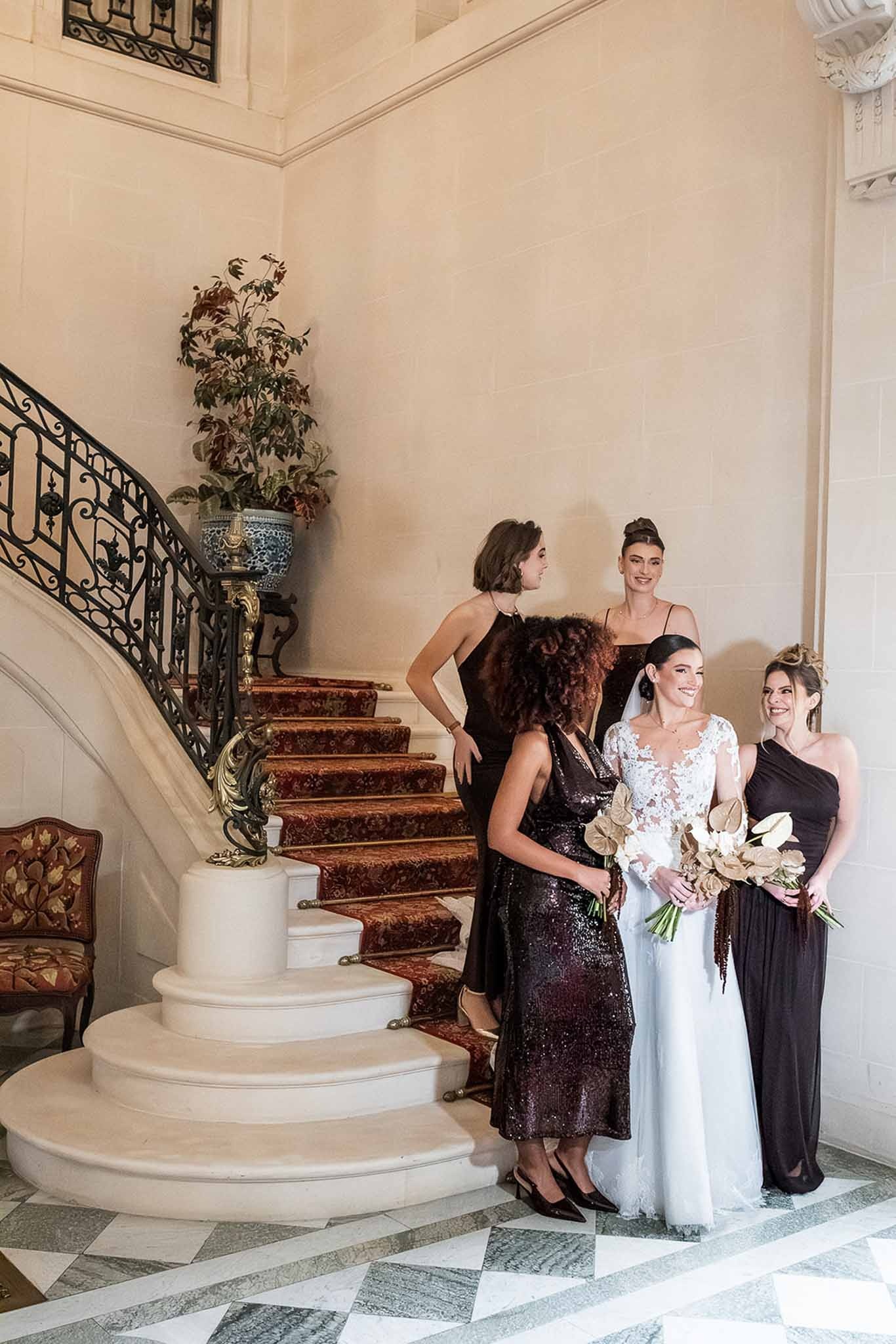 Bride with bridesmaids in dark gowns on grand staircase at Chateau du Terral