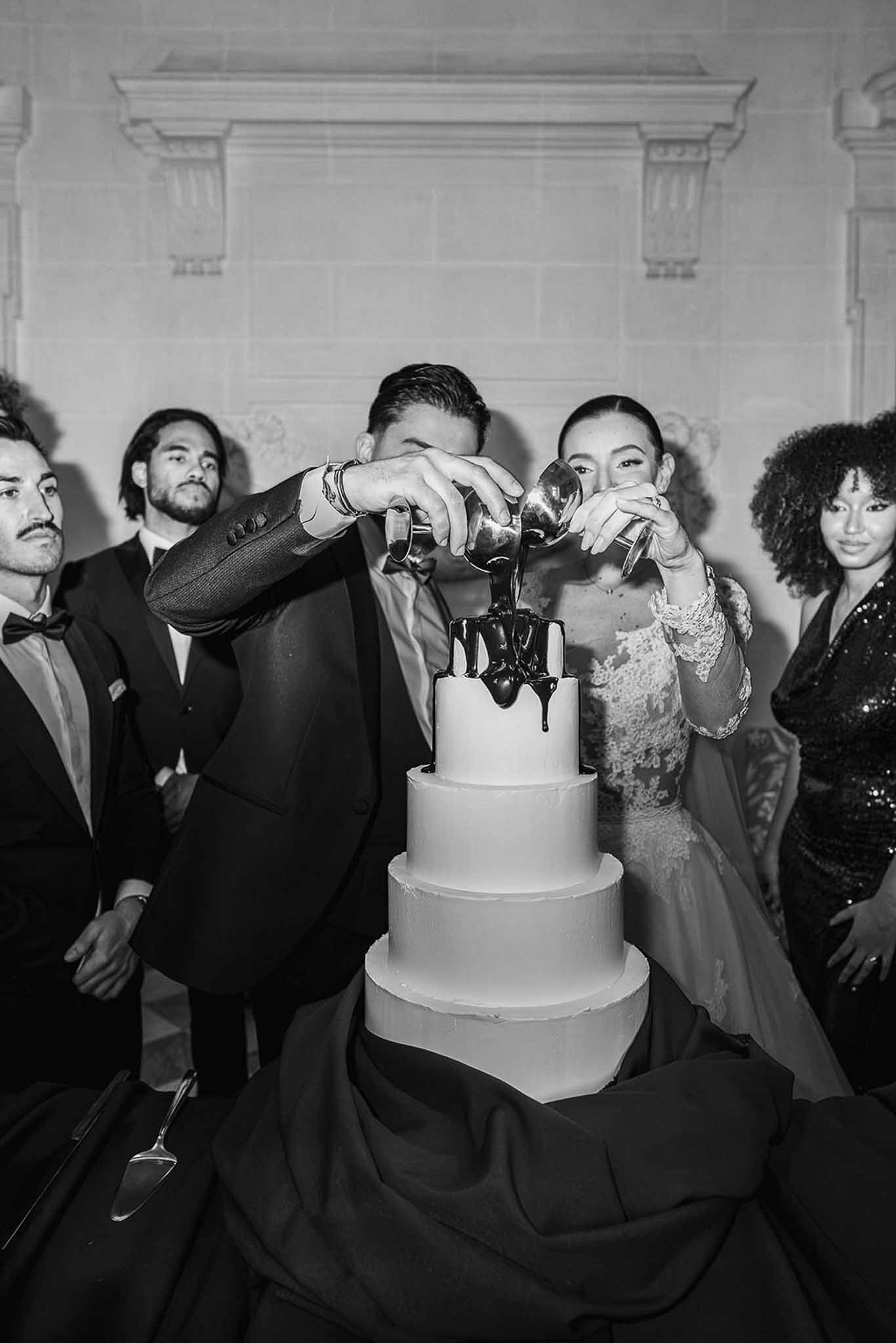 Groom pouring chocolate over wedding cake at Chateau du Terral in black and white
