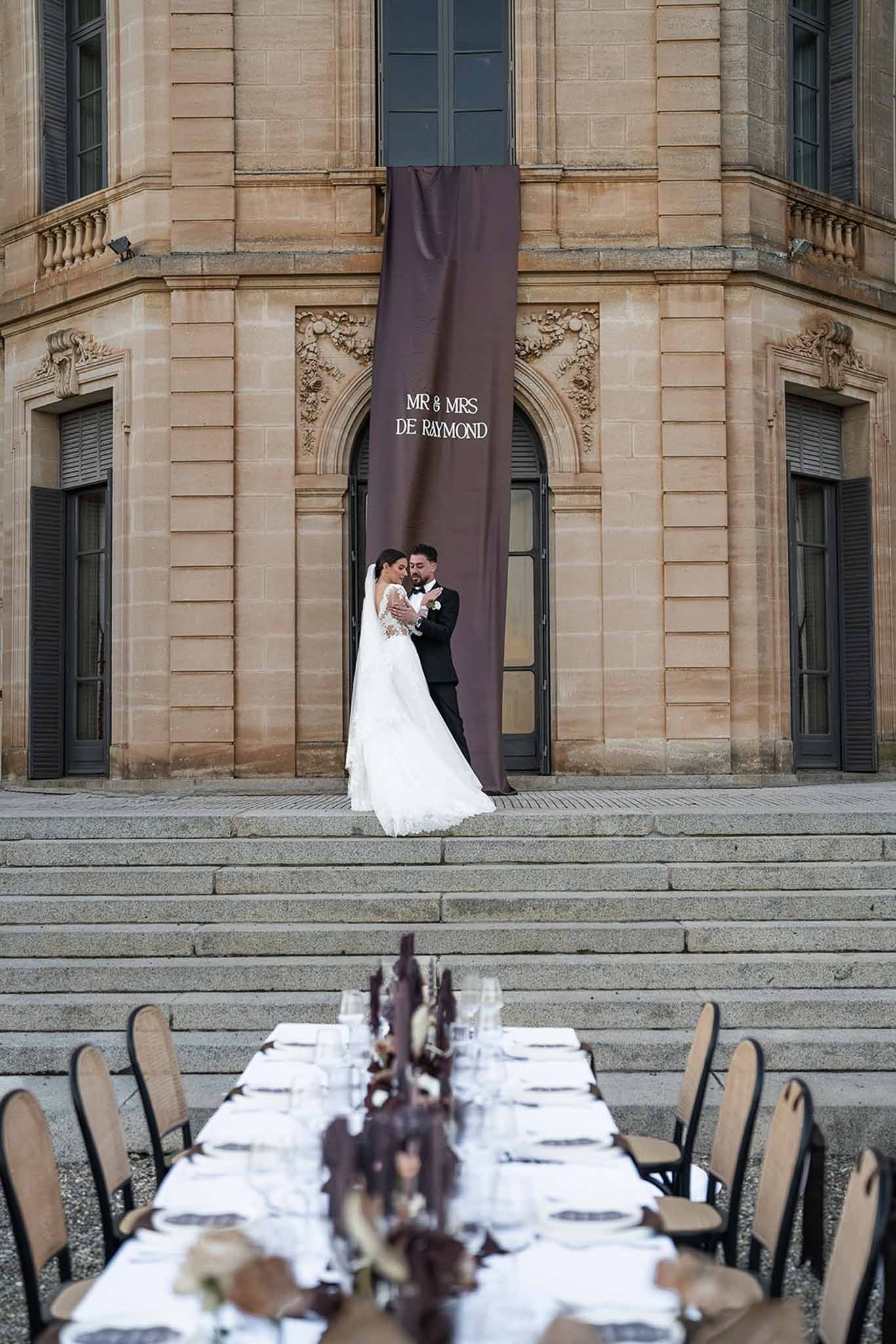 Couple embracing on chateau steps with reception table at Chateau du Terral